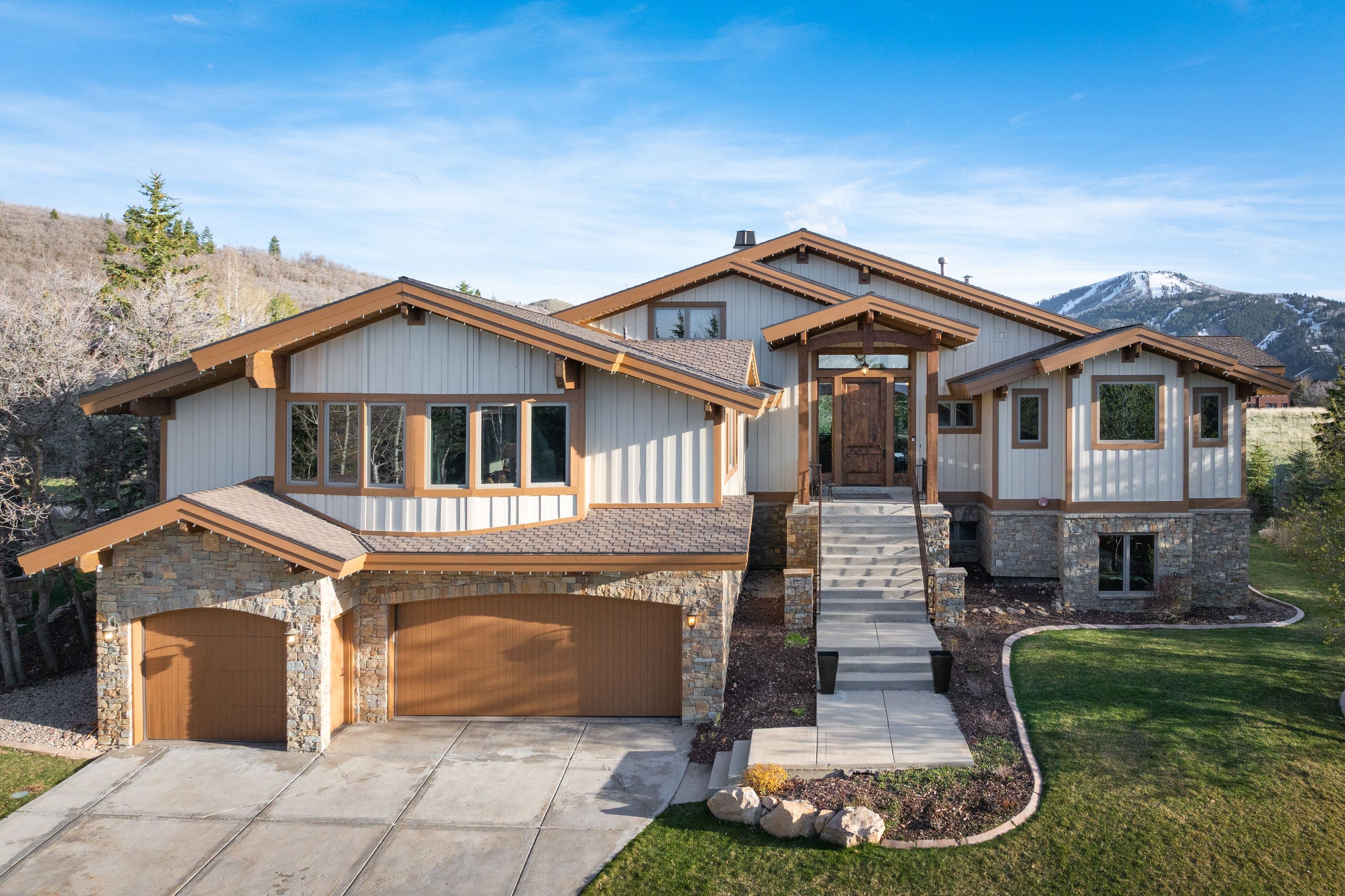 View of front of home with an attached garage, driveway, stone siding, a front lawn, and a mountain view