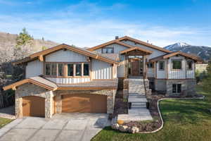 View of front of home with an attached garage, driveway, stone siding, a front lawn, and a mountain view