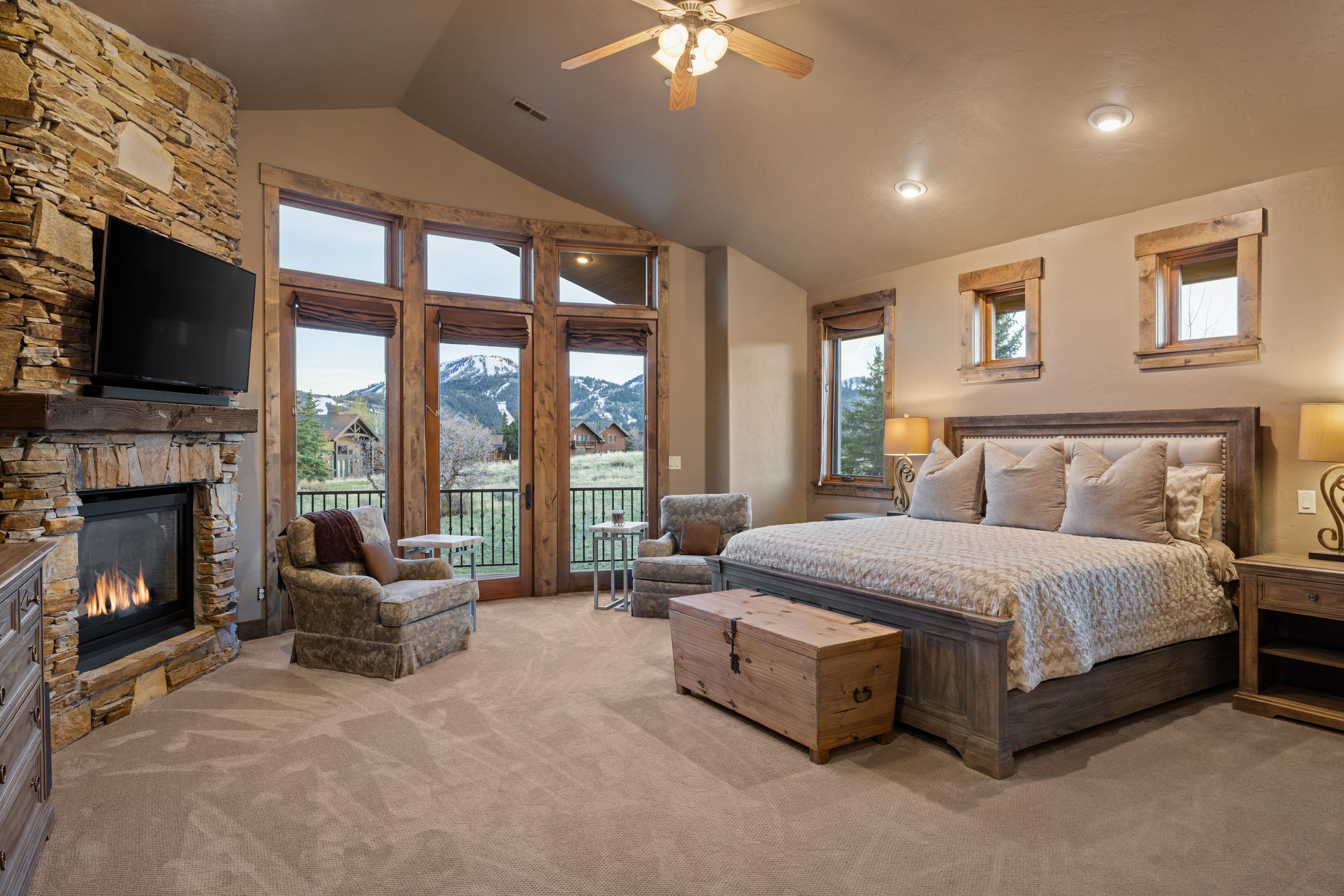 Carpeted bedroom with access to exterior, a stone fireplace, a ceiling fan, and a high ceiling