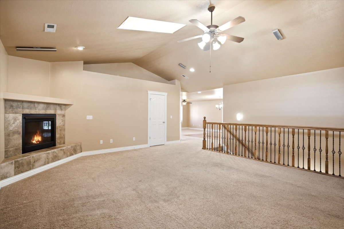 Carpeted living area featuring a stone-surround fireplace with hearth, vaulted ceilings, and a skylight