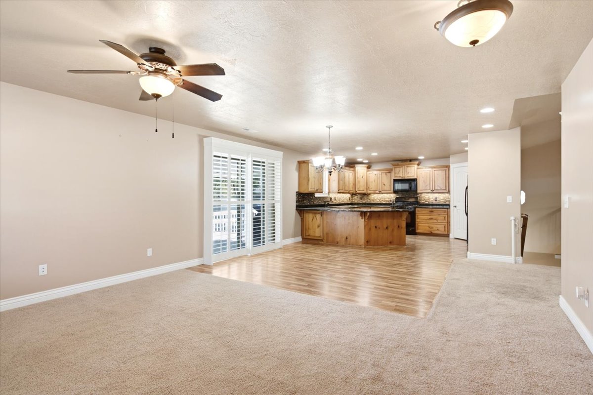 Open-concept living space featuring a ceiling fan, sliding glass doors with plantation shutters, wood-finish flooring, a kitchen with wood cabinetry, and recessed lighting