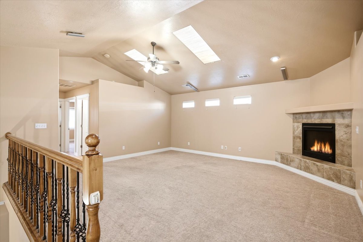 Spacious room featuring vaulted ceilings with skylights, a ceiling fan, and a gas fireplace with a tiled surround