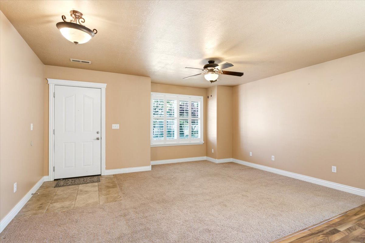 Entryway and living area featuring a neutral color palette, carpet flooring, a window with plantation shutters, a ceiling fan, and tile flooring at the entry