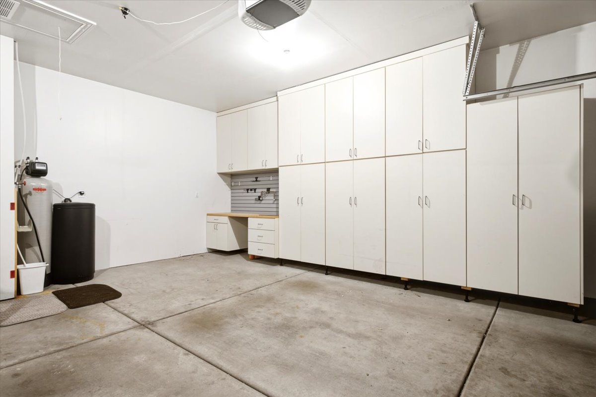 Garage featuring extensive built-in white cabinetry, workbench with light wood-finish countertop, organized pegboard, and utility sink