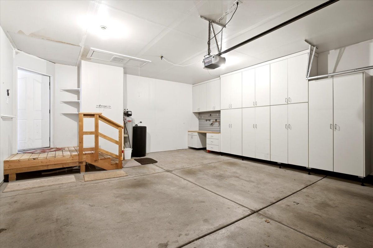 Integrated garage featuring extensive white cabinetry, a built-in workbench, an automatic garage door opener, a wooden entry platform with railing, and a side access door
