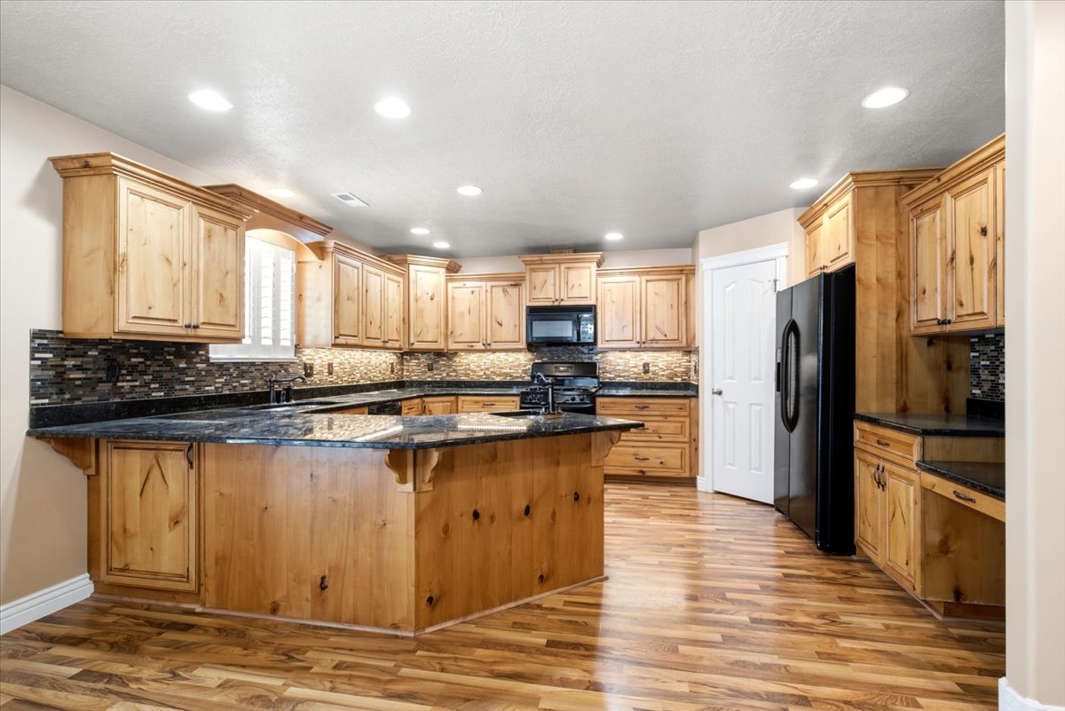 Spacious kitchen featuring extensive wood cabinetry, dark countertops, a large central island, black appliances, and wood-finish flooring