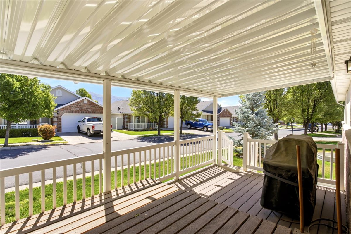 Covered outdoor patio featuring a slatted wood-finish deck, white railing, and a corrugated metal roof