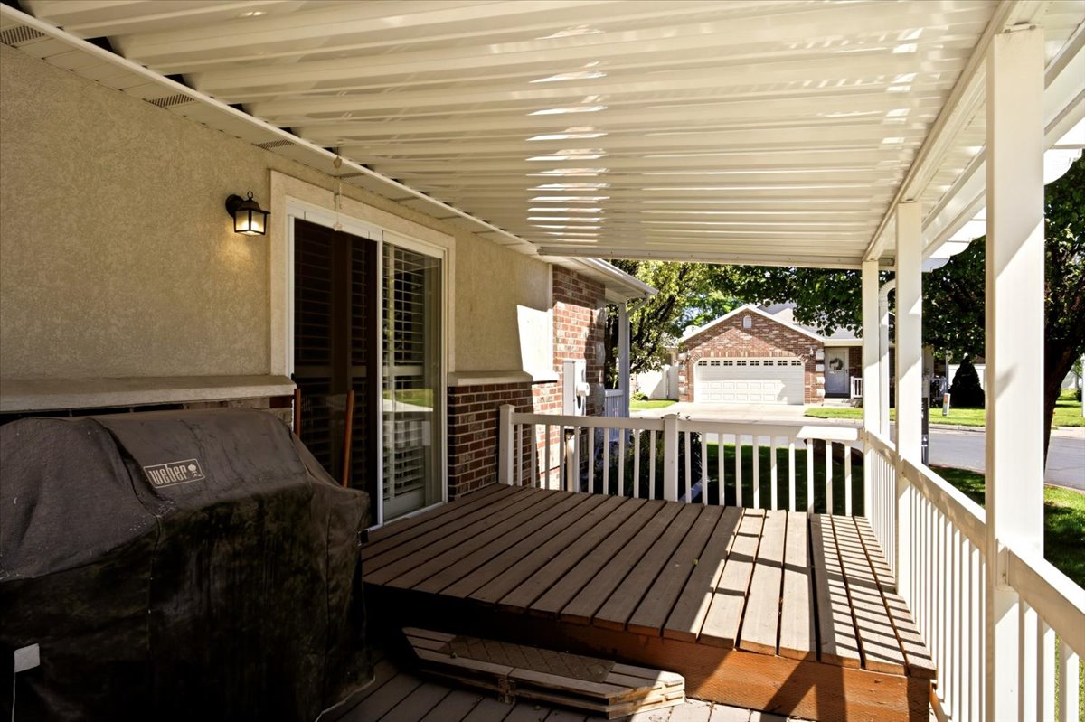 Covered patio featuring a wood-finish deck with white railing, stucco exterior, and a sliding glass door