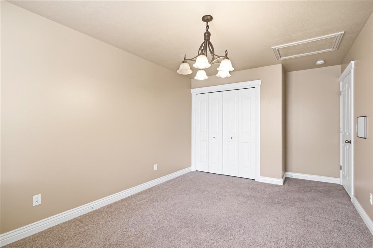 Carpeted room featuring a ceiling-mounted chandelier, white bi-fold closet doors, white baseboards, and a white interior door