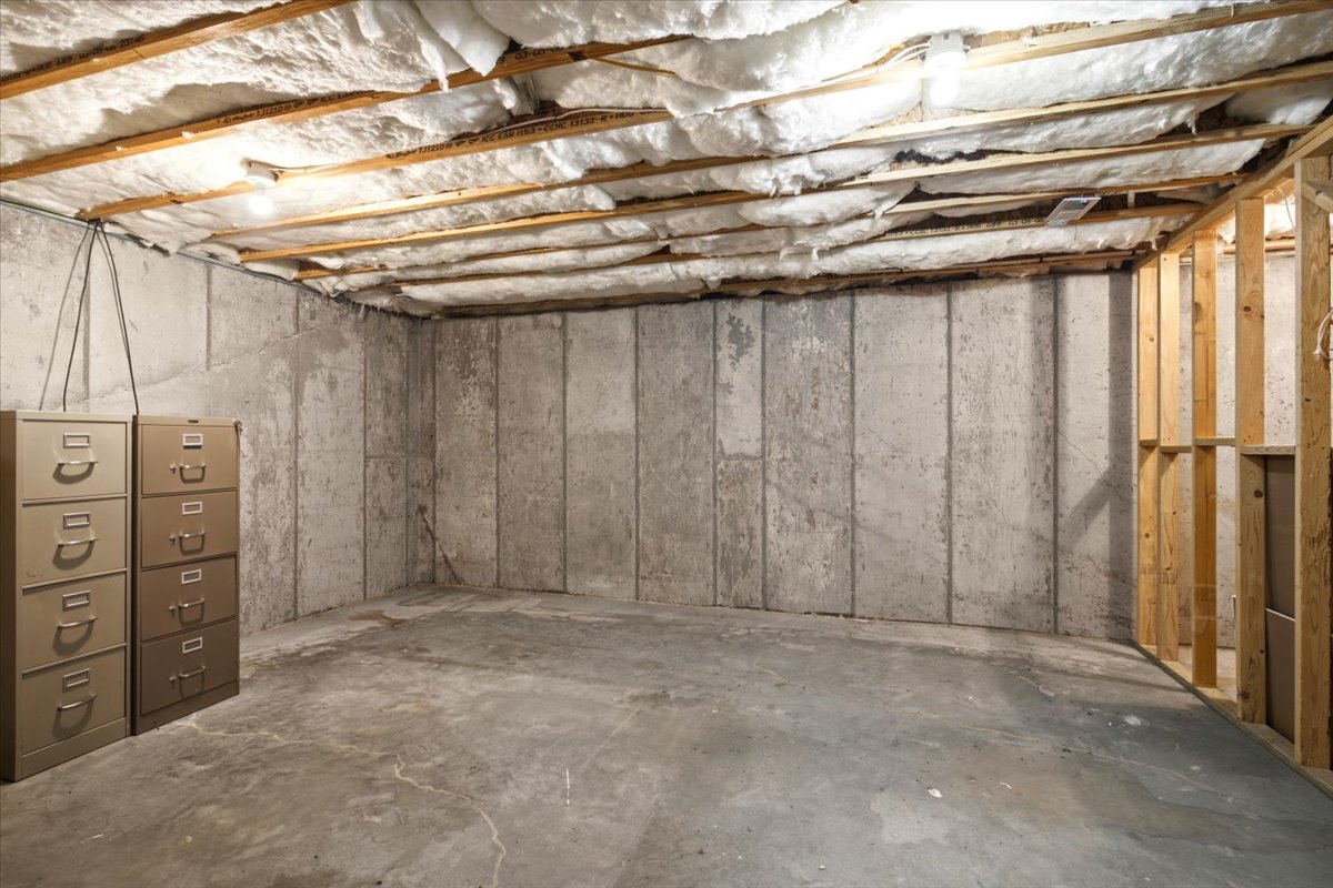 Unfinished basement space featuring exposed ceiling joists with insulation, concrete slab flooring, and concrete foundation walls
