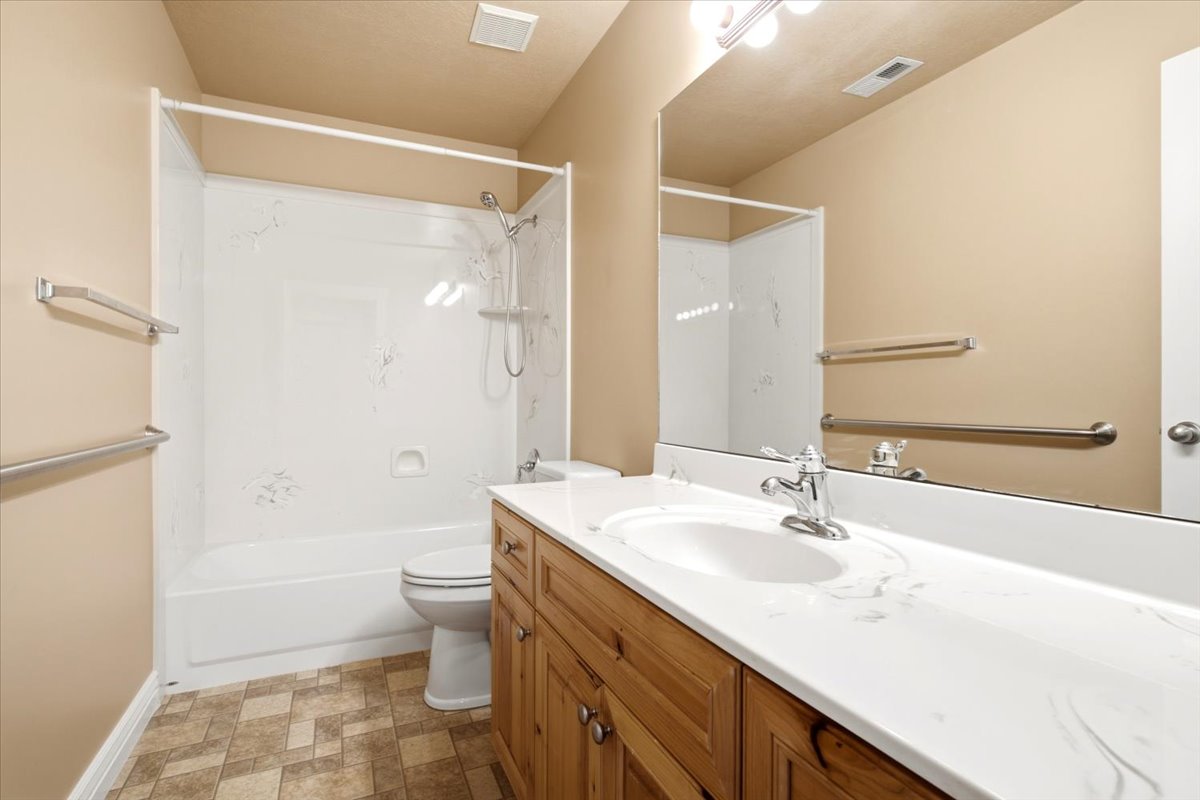 Bathroom featuring a white bathtub and shower surround, a wood-finish vanity with a white countertop and integrated sink, a chrome faucet, and patterned floor tile