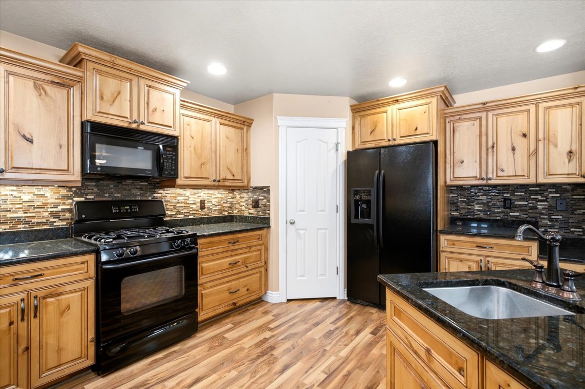 Kitchen featuring wood-finish cabinetry, black appliances, dark countertops, and a mosaic tile backsplash
