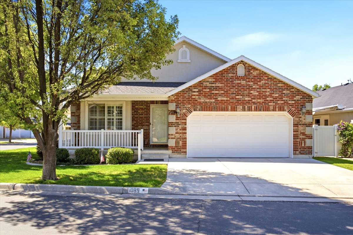 Brick and stucco exterior featuring a two-car garage, covered porch with white railing, and a manicured lawn