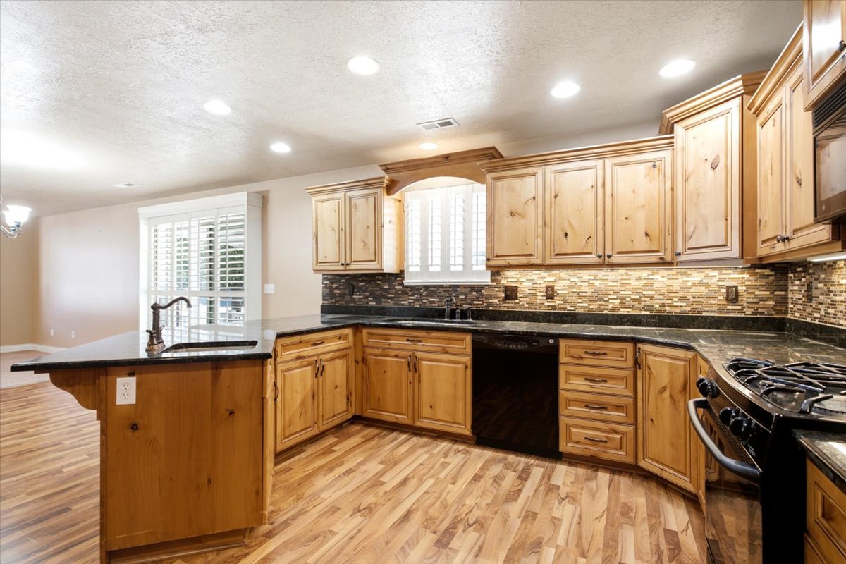 Spacious kitchen featuring a large island with a sink, light wood cabinetry, dark countertops, a tiled backsplash, and recessed lighting