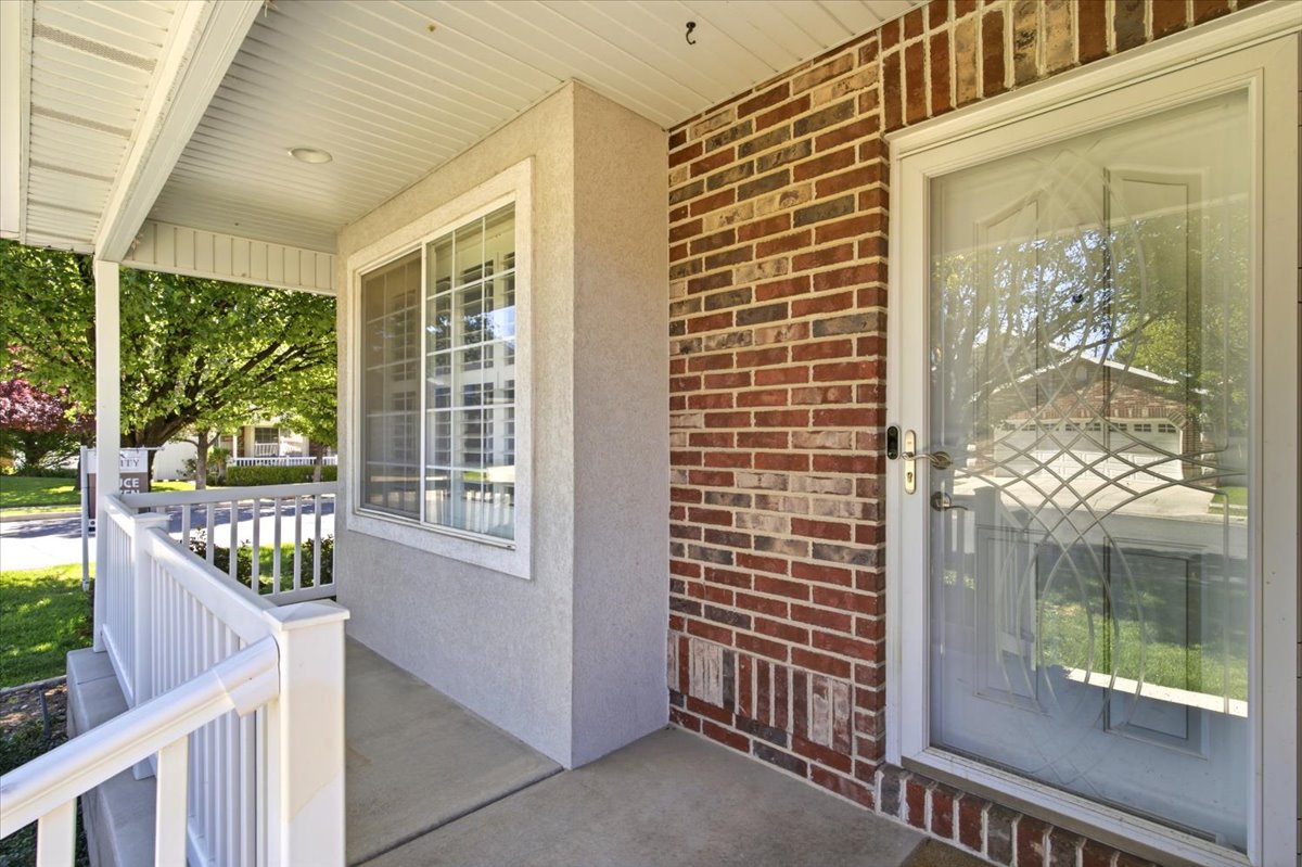 Covered front porch featuring stucco and brick siding, white railing, and a storm door with decorative glass