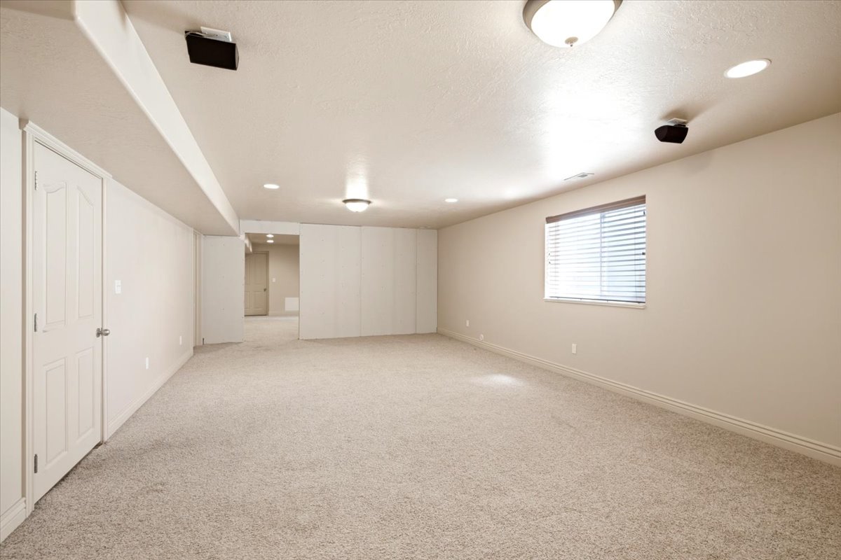 Spacious carpeted room featuring recessed lighting, a built-in speaker system, and a window with horizontal blinds