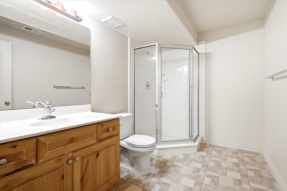 Bathroom featuring a corner shower enclosure with clear glass, a vanity with a light wood finish, a white countertop, and patterned floor tiles
