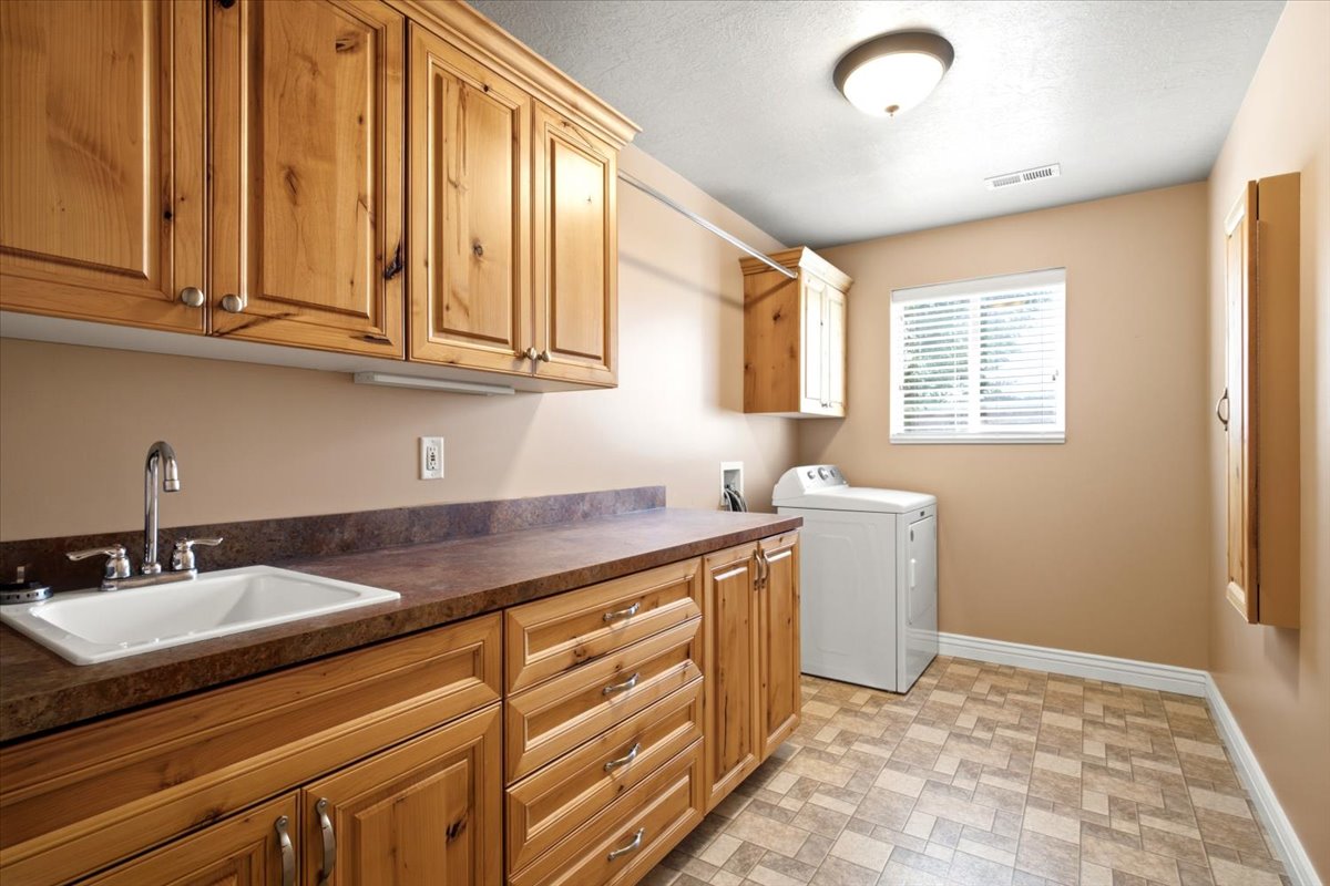 Laundry room featuring extensive wood cabinetry, a utility sink with chrome faucet, and ample countertop space