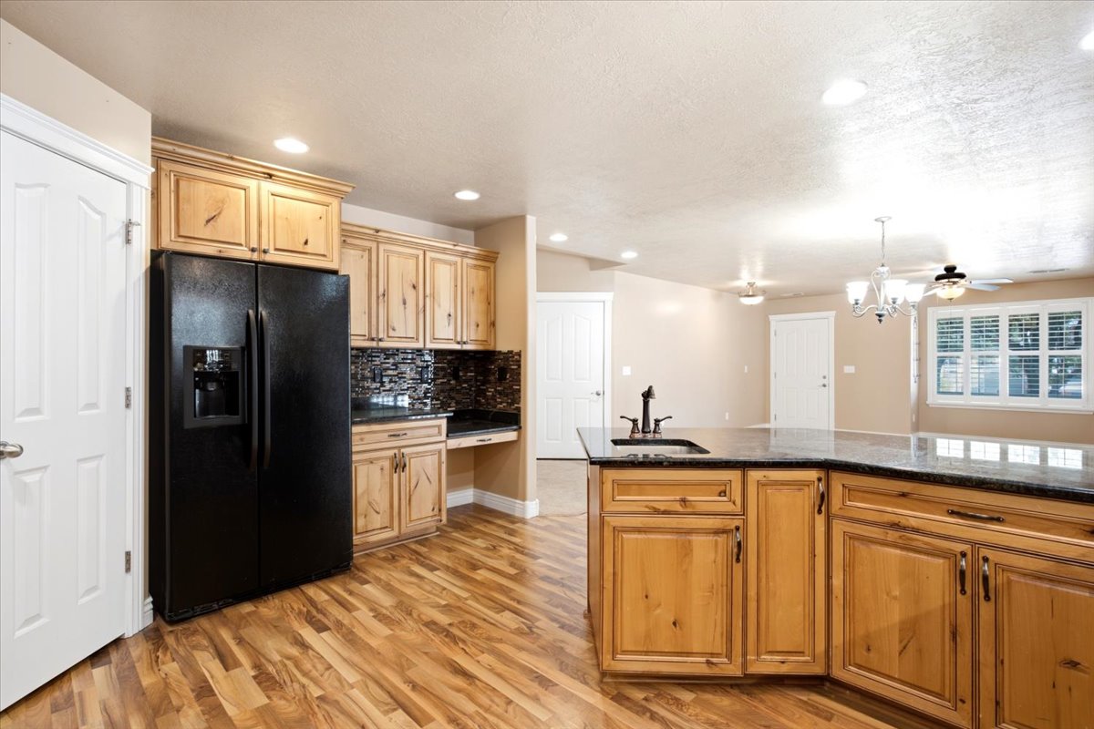 Kitchen featuring natural wood cabinetry, dark countertops, wood-finish flooring, a mosaic tile backsplash, and recessed lighting