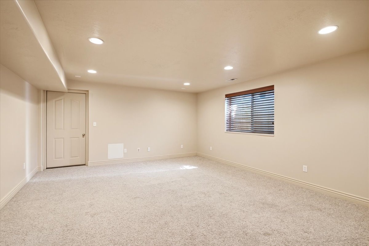Spacious room featuring neutral carpeting, a single window with horizontal blinds, recessed ceiling lighting, and a white paneled door