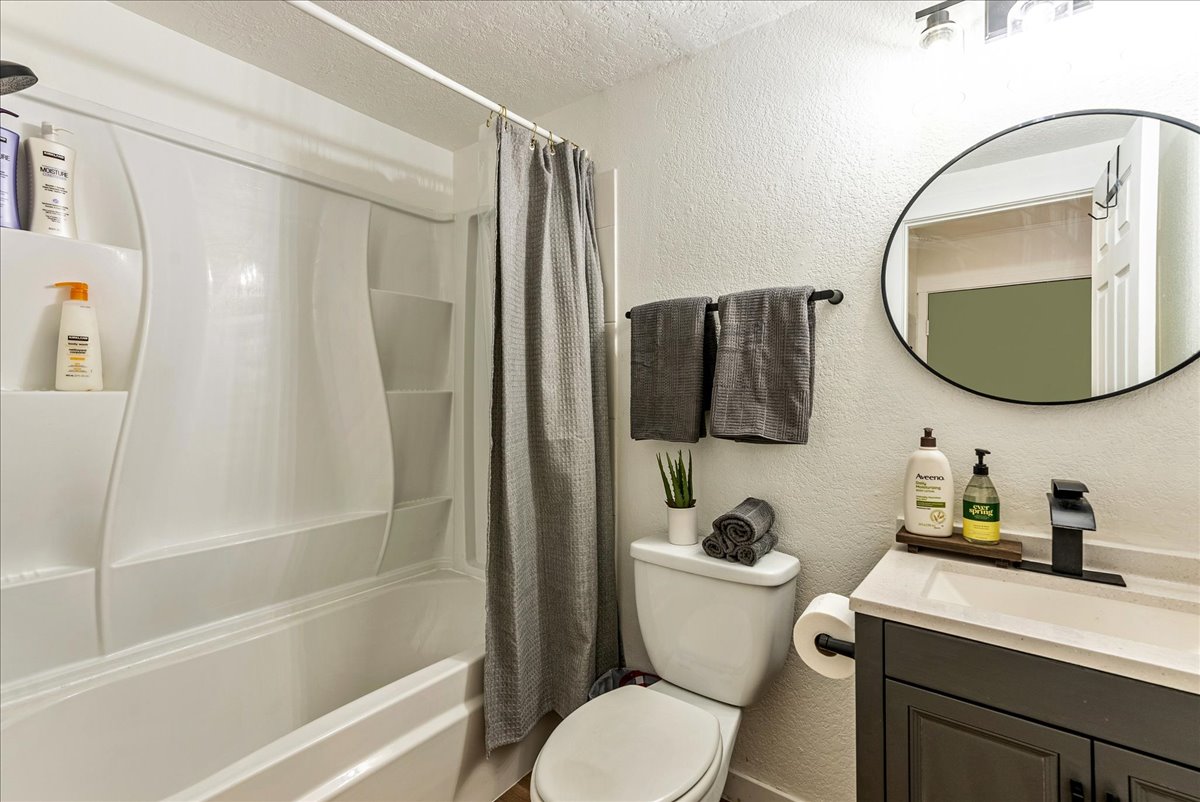 Bathroom featuring a white tub/shower combination, dark gray vanity with a single sink, black faucet, and a circular mirror