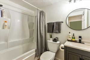 Bathroom featuring a white tub/shower combination, dark gray vanity with a single sink, black faucet, and a circular mirror