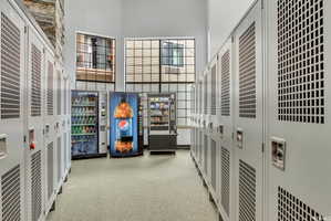 Corridor featuring rows of light gray lockers, high ceilings, and multiple windows