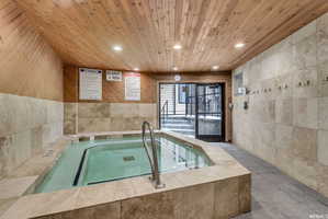 Indoor spa featuring a tiled surround, wood-finish ceiling, recessed lighting, and access to exterior stairs