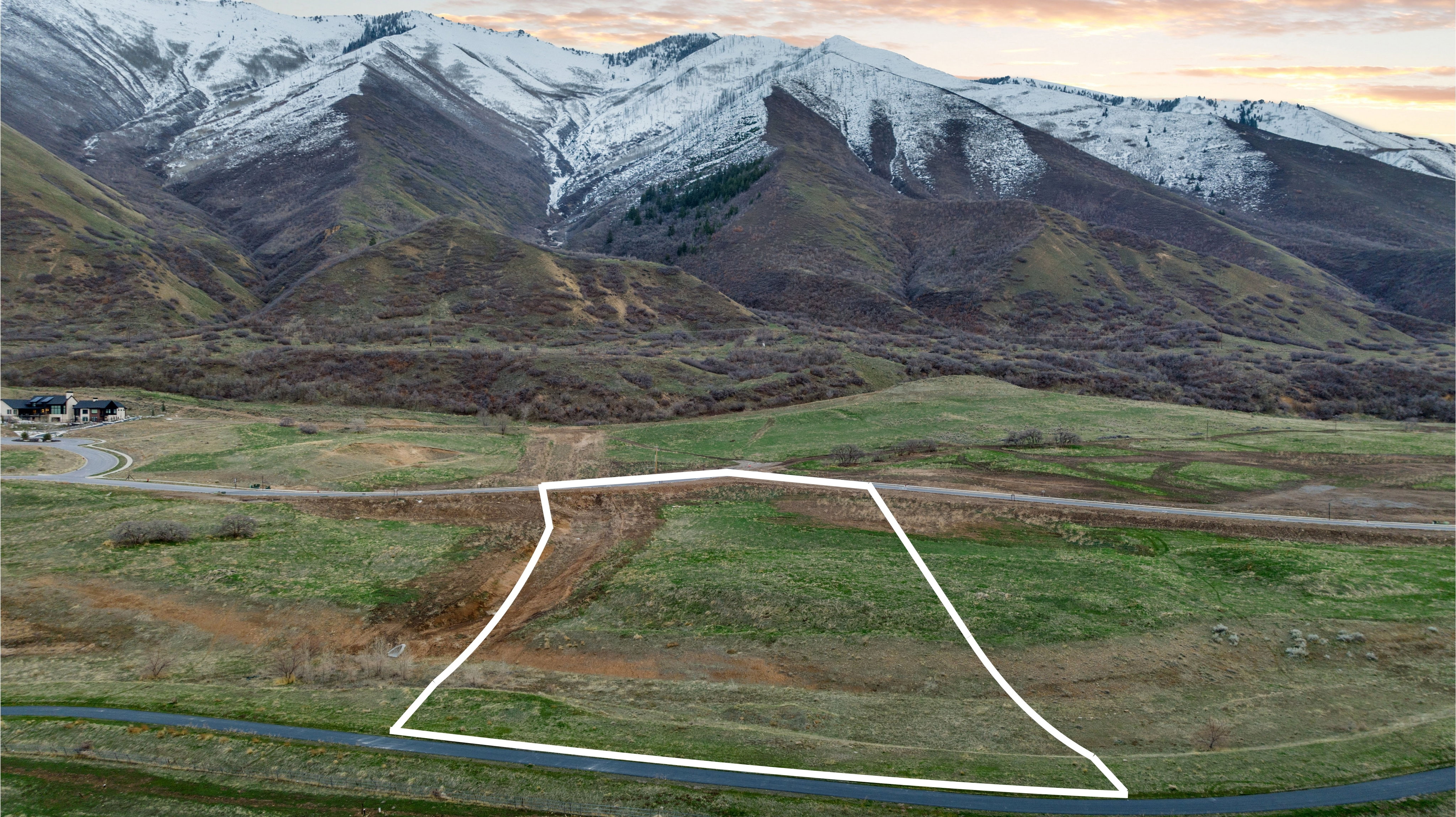 Expansive land parcel featuring a gentle slope, mature mountain backdrop, and direct paved road frontage