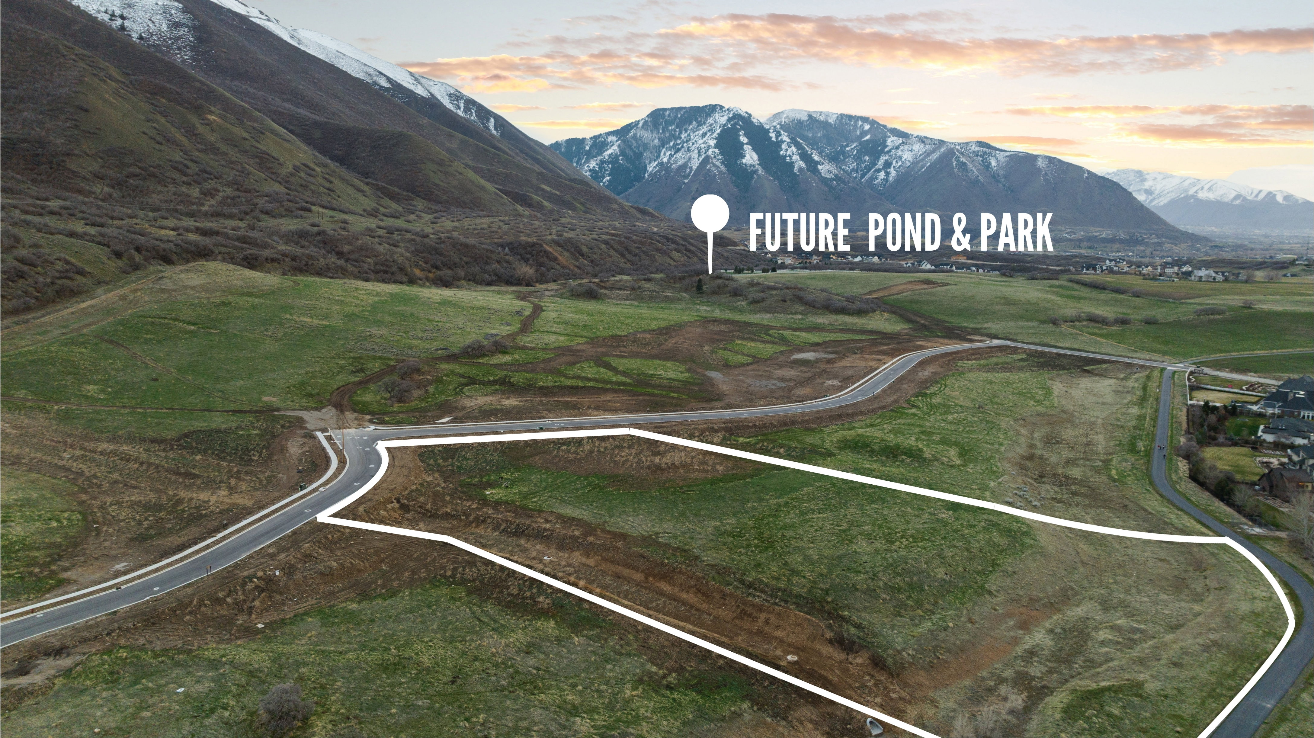 Expansive land parcel featuring established roadways, surrounding green space, and a mountainous backdrop