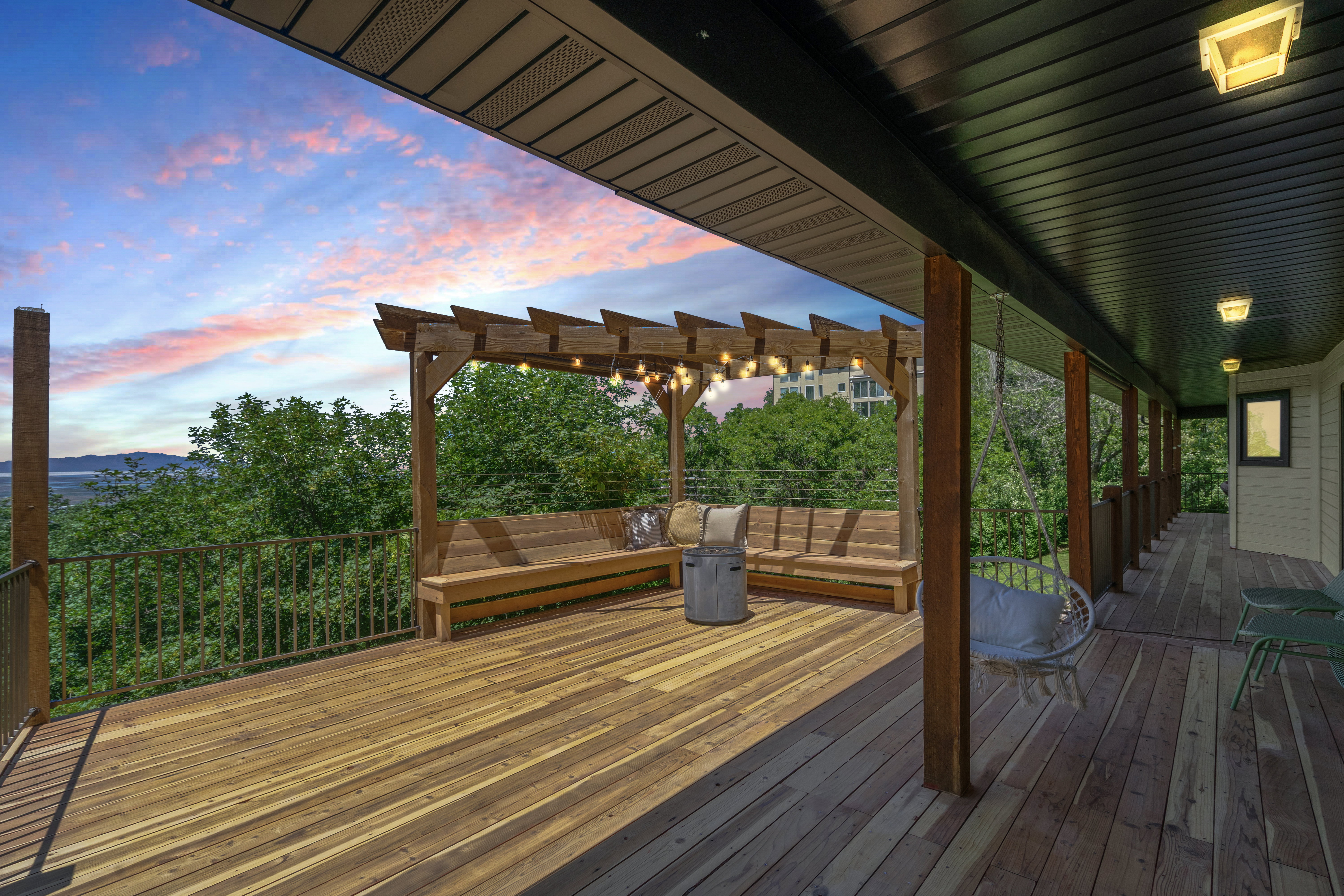 Expansive outdoor deck featuring wood-finish flooring, a pergola with string lighting, and built-in bench seating