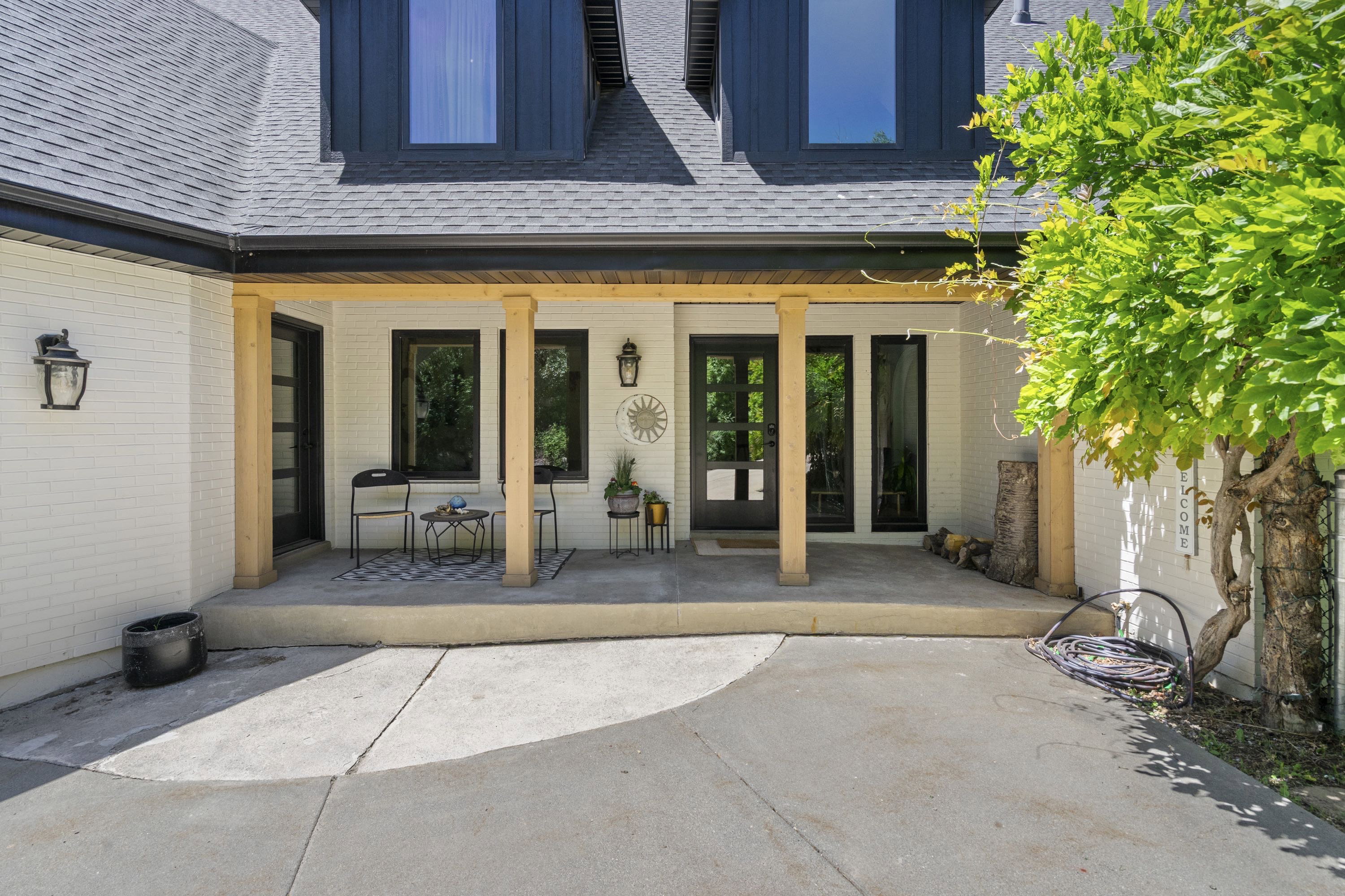 Covered entry with natural wood-tone pillars, white brick facade, and black trim windows