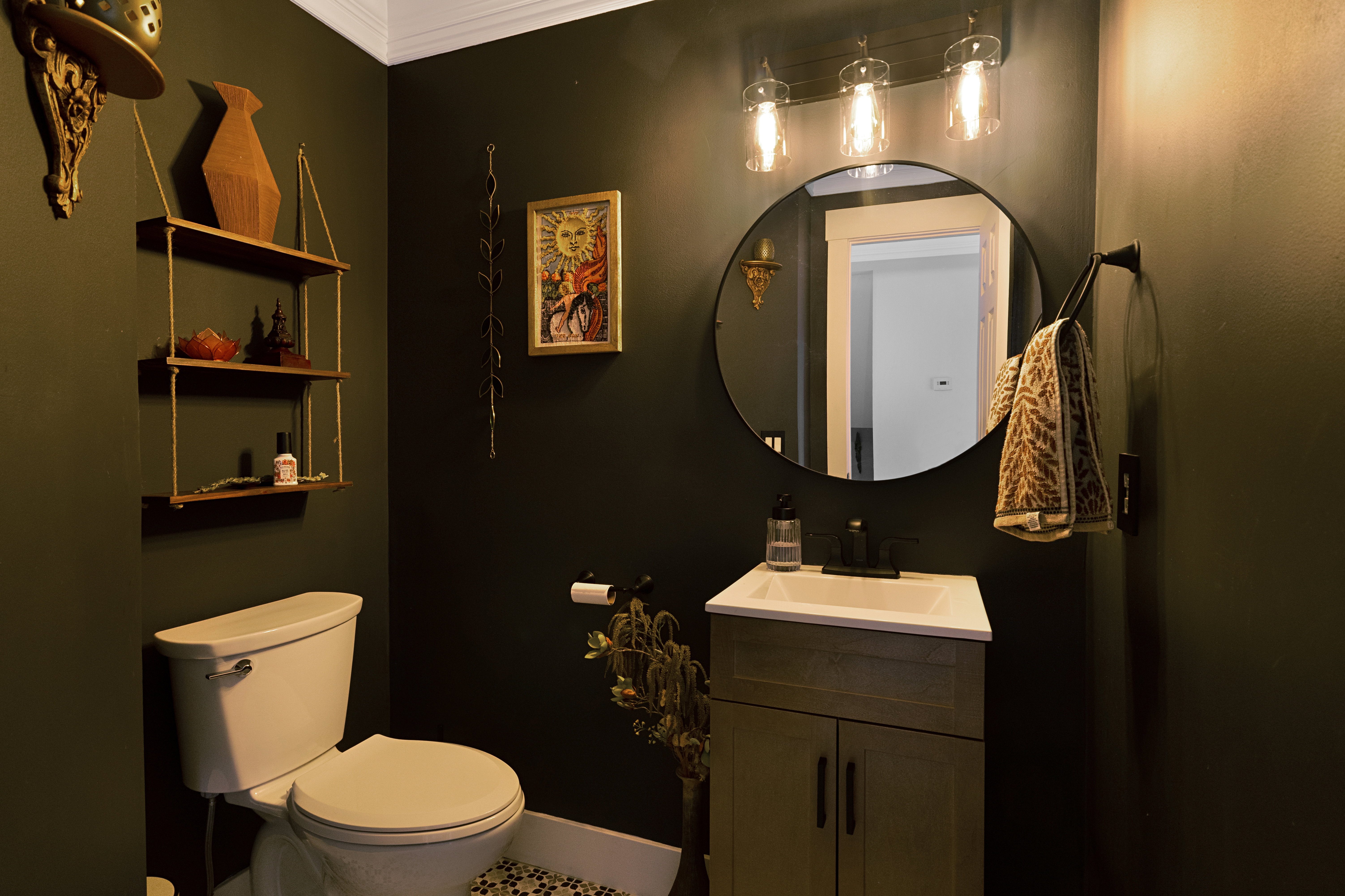 Well-appointed powder room featuring a circular mirror, a vanity with under-sink storage, a modern three-light fixture, and a mosaic tile floor