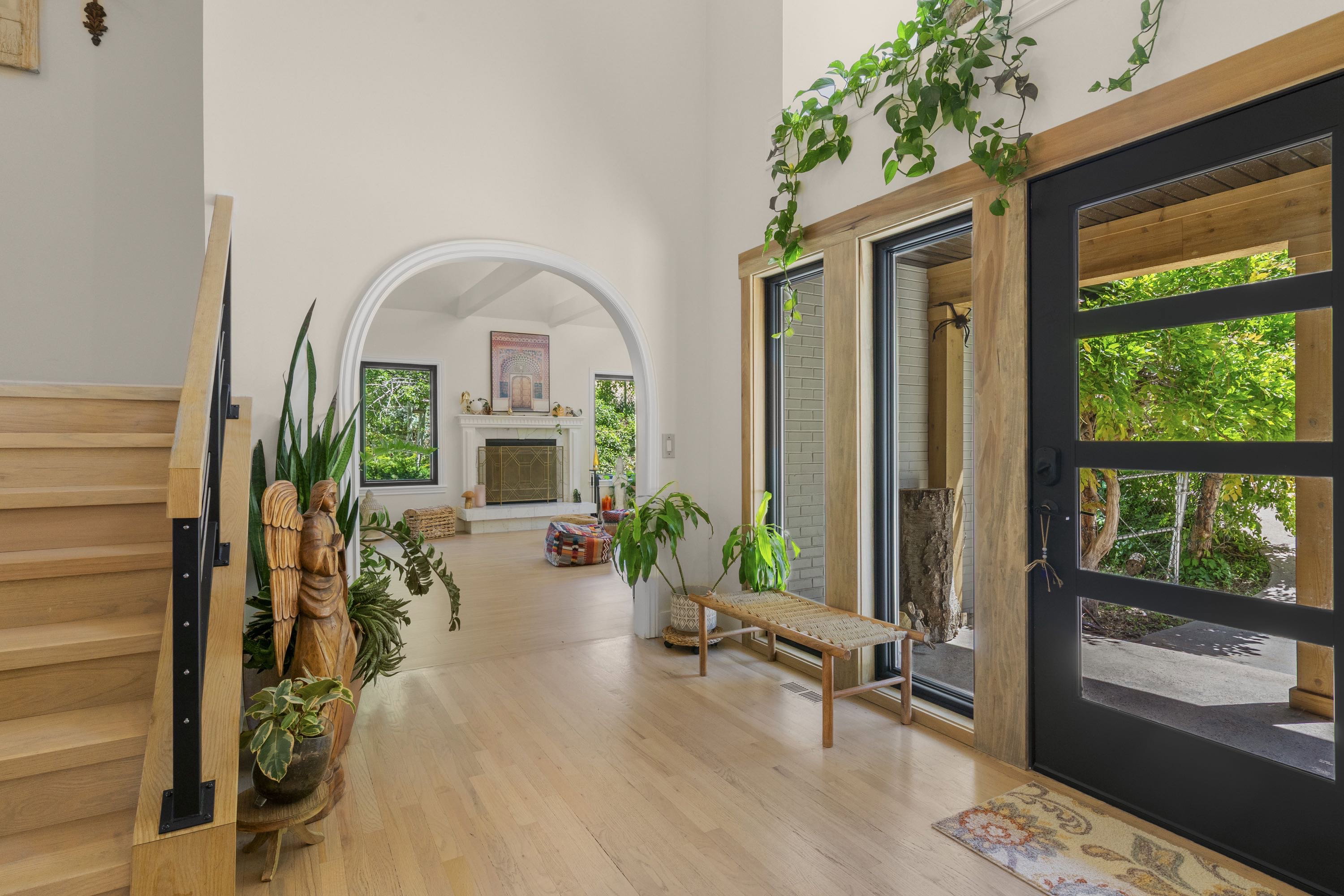 Modern entryway featuring a black panel-glass door, light wood-finish flooring, and a contemporary staircase with black metal balusters