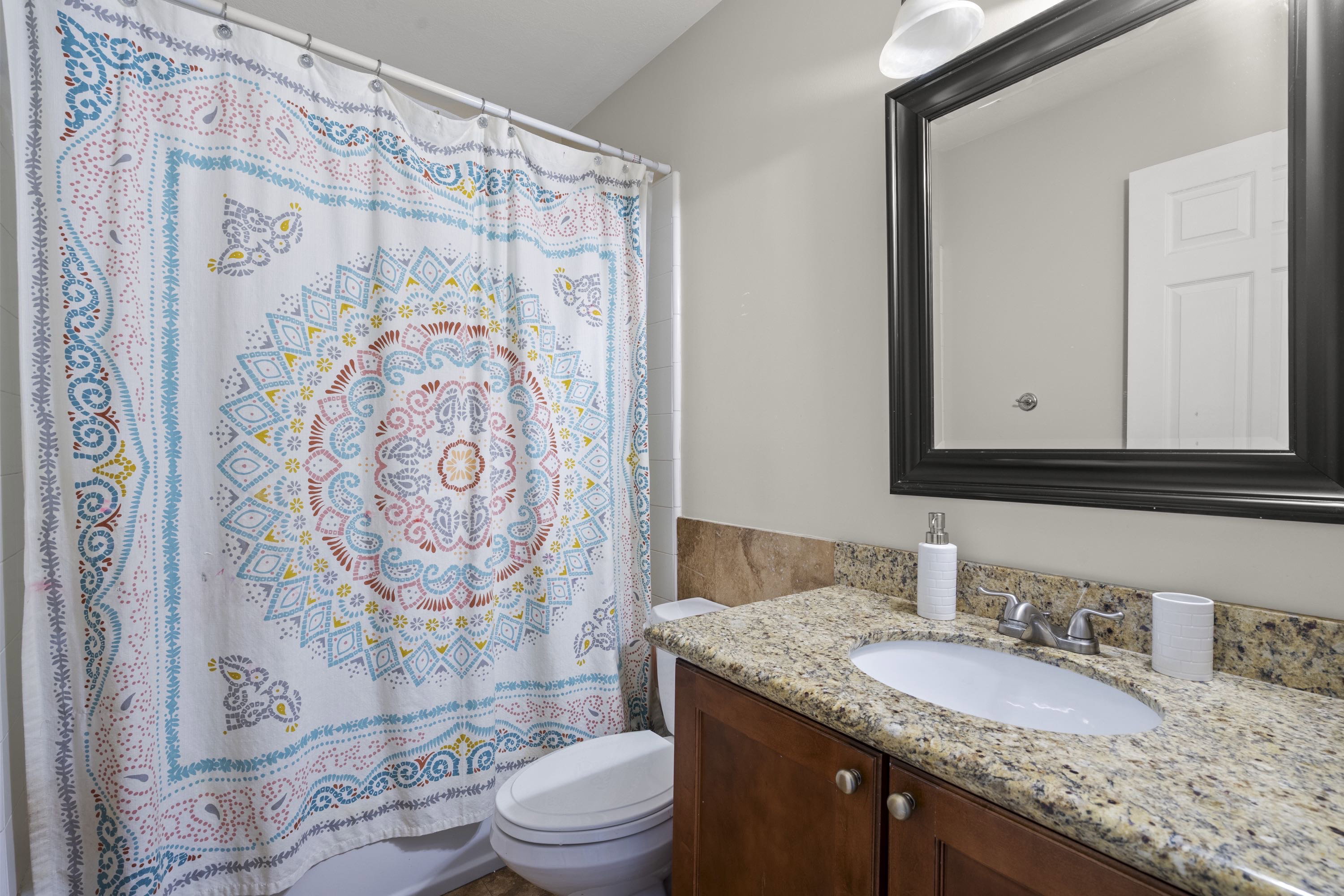 Bathroom featuring a vanity with a light-toned granite countertop, undermount sink, dark wood-finish cabinetry, and a framed mirror