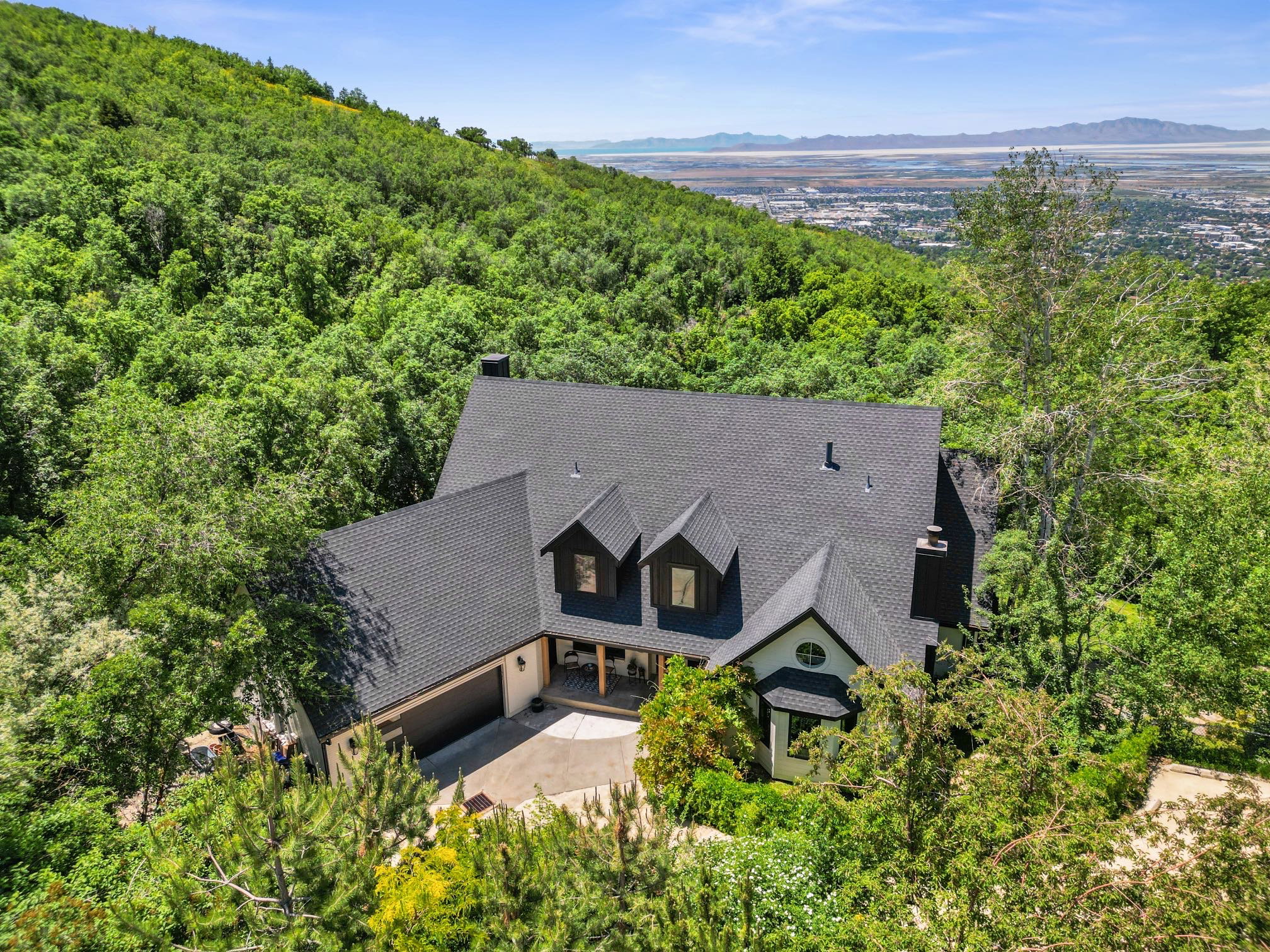 Hillside residence featuring a dark shingle roof, white exterior with black trim, an attached garage, and multiple dormer windows