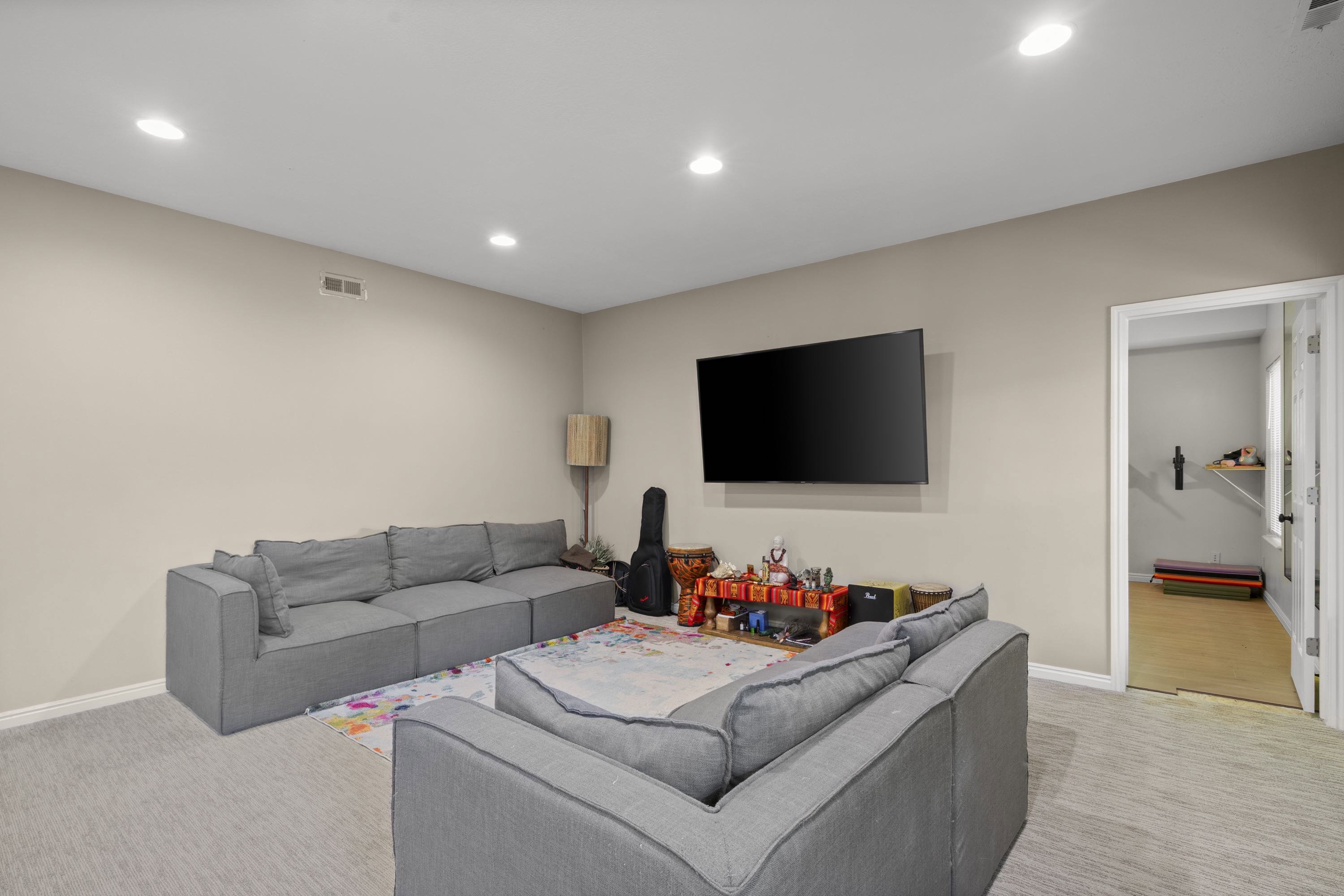 Recessed ceiling lighting illuminates this versatile room, featuring light neutral wall paint and plush carpeting