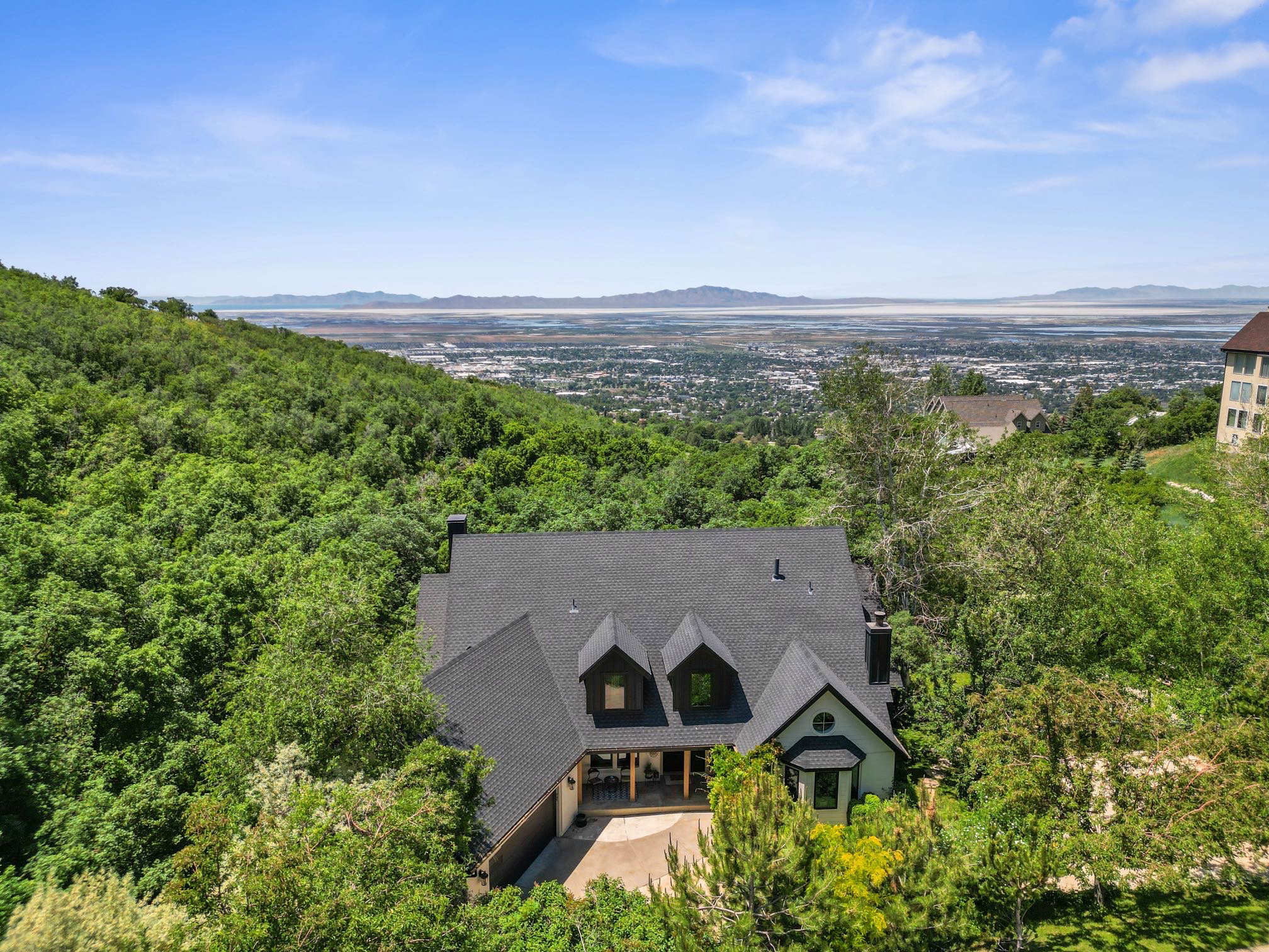 Hillside residence featuring a dark shingle roof, multiple dormer windows, a prominent bay window, and an attached garage