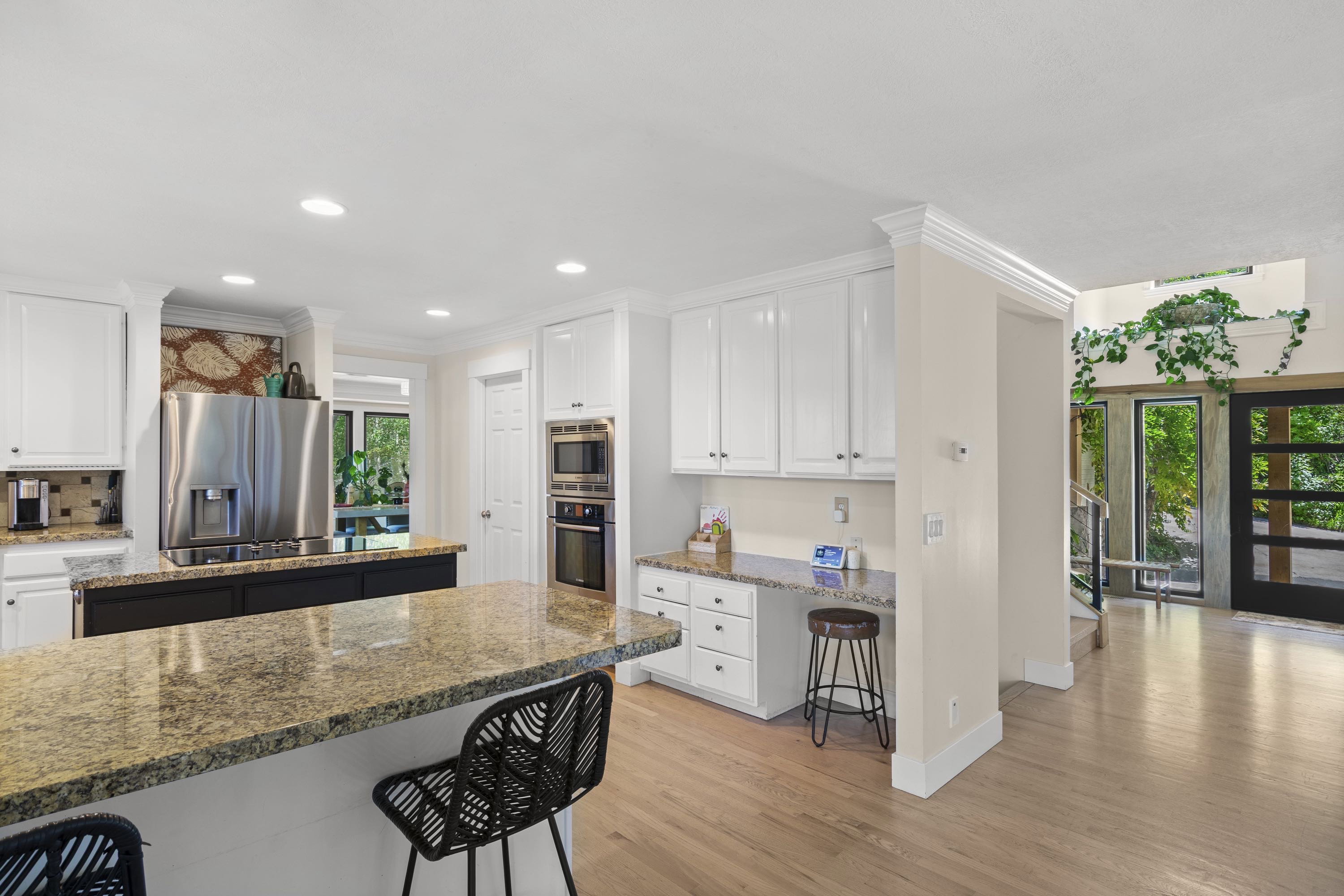 Kitchen featuring an expansive stone countertop island, stainless steel appliances, white cabinetry, wood-finish flooring, and a built-in desk area