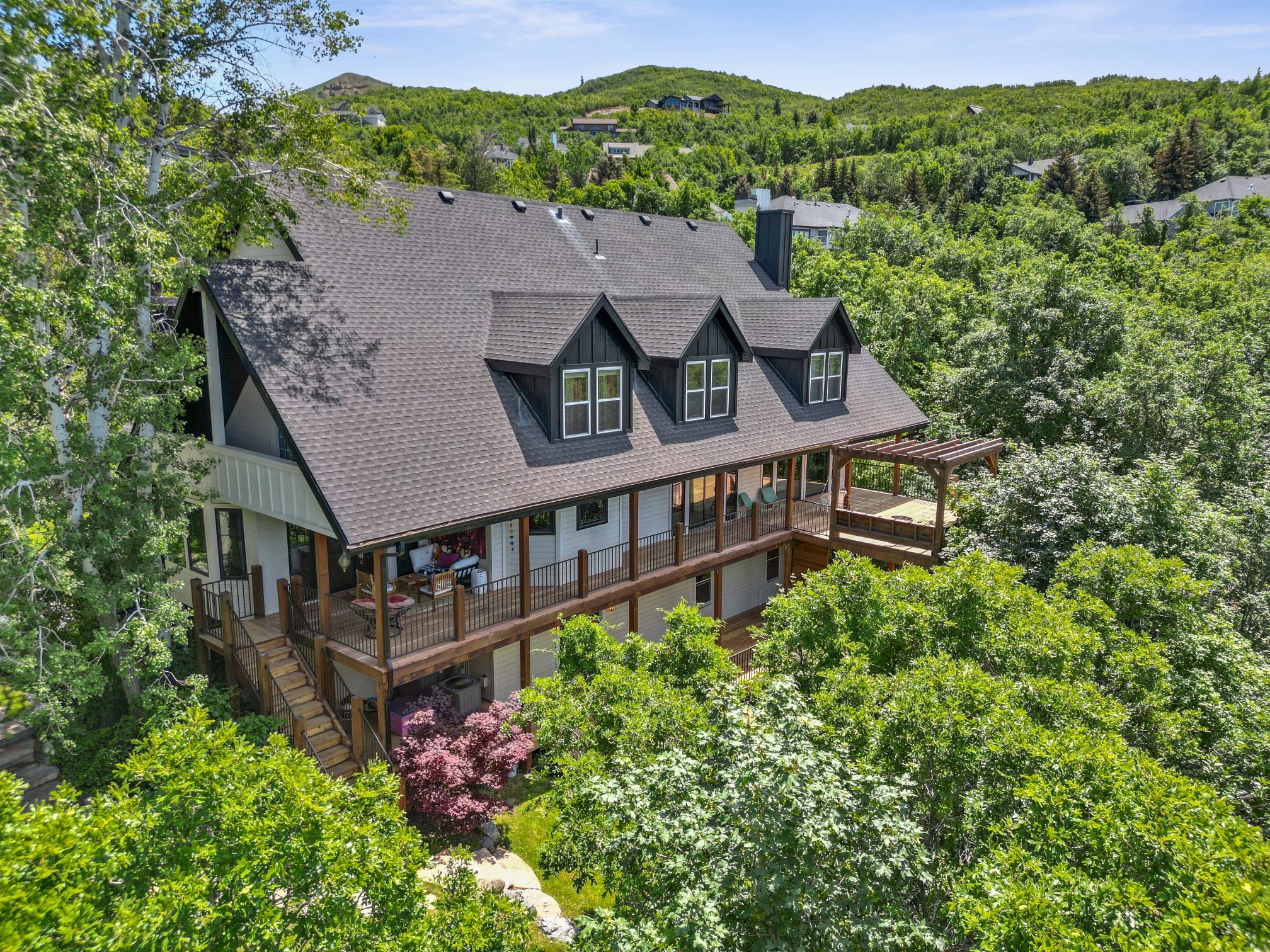 Multi-level residence featuring a dark shingle roof, dormer windows, and white vertical siding