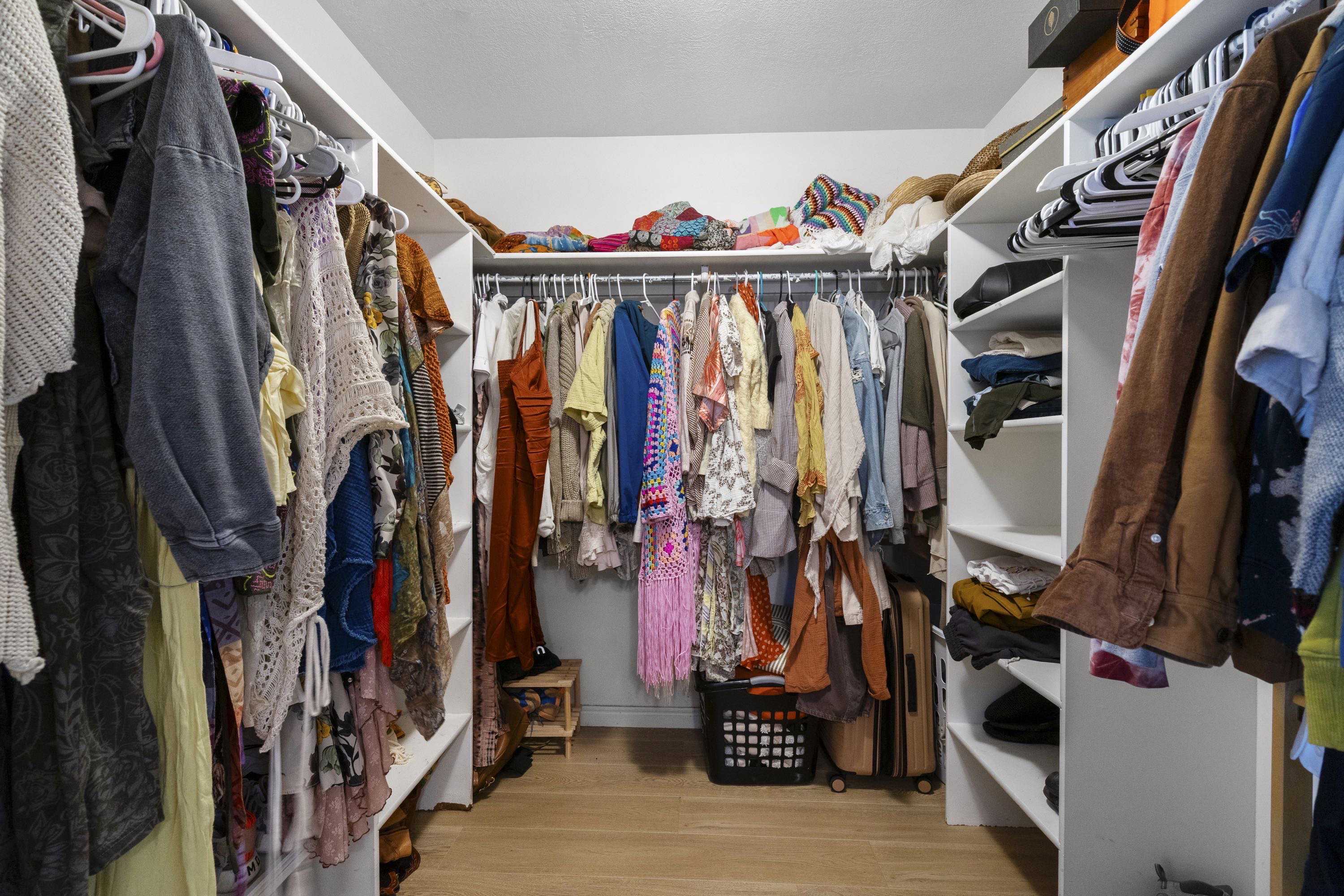 Walk-in closet with L-shaped shelving system, multiple hanging rods, and wood-finish flooring