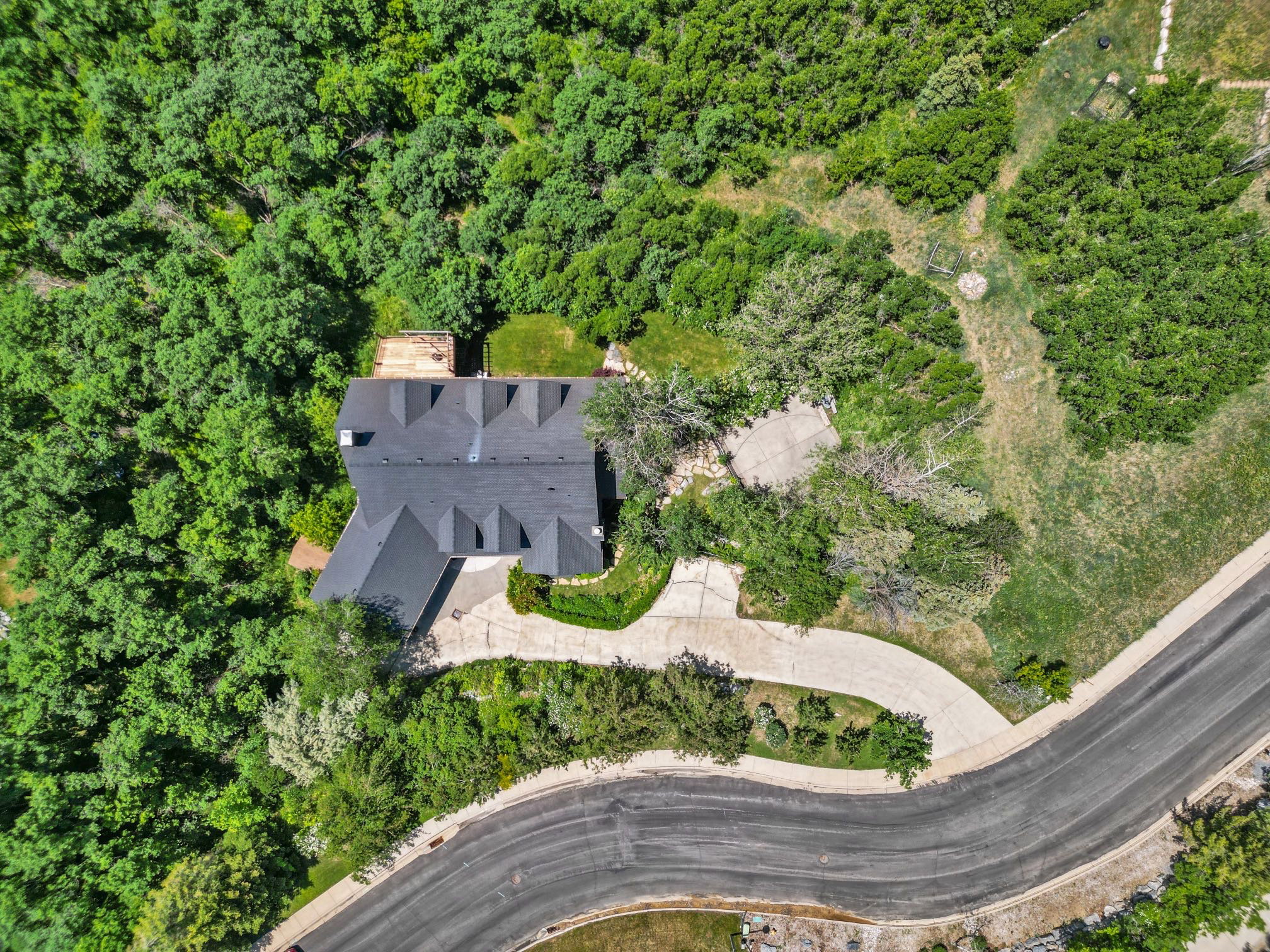 Expansive property featuring a curved asphalt road, a private paved driveway, and a multi-peaked roofline