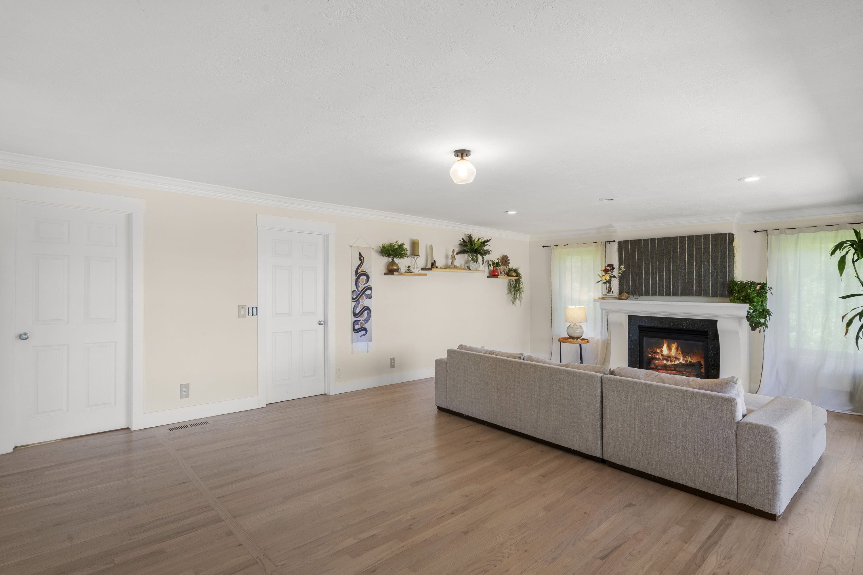 Spacious room featuring wood-finish flooring, a white mantel fireplace, multiple windows with white sheer curtains, and two white paneled doors