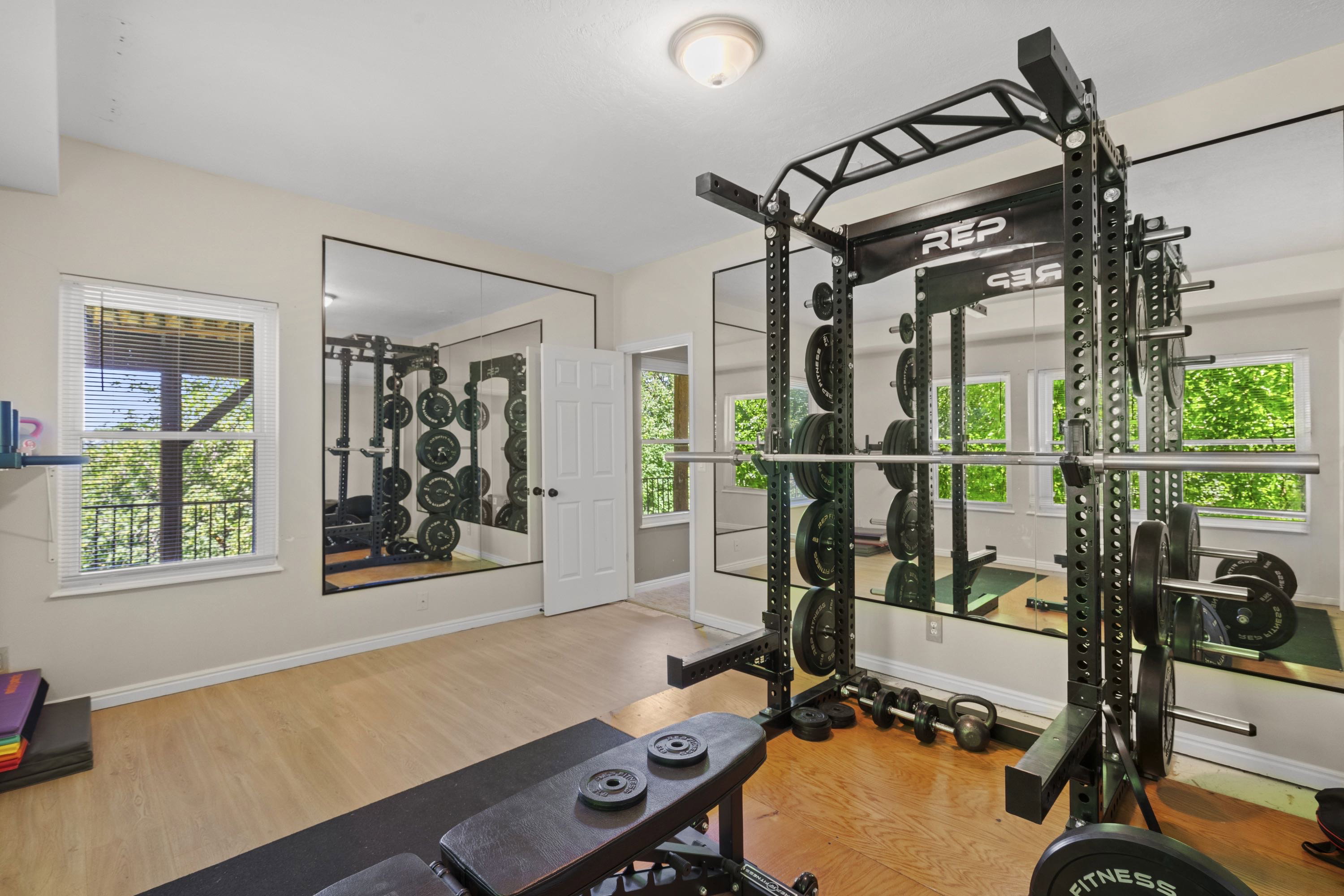 Dedicated fitness room featuring light wood-finish flooring, a full wall of reflective mirrors, and multiple windows