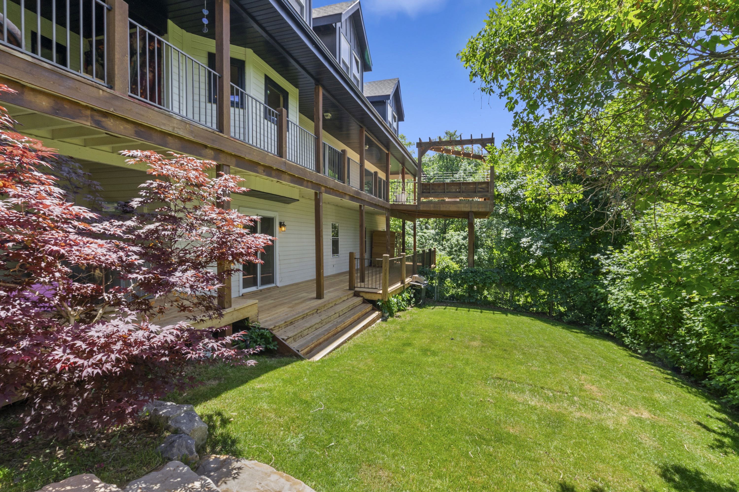 Multi-level exterior decks with wood railings, a lower-level patio, and a tiered wooden staircase leading to a manicured lawn