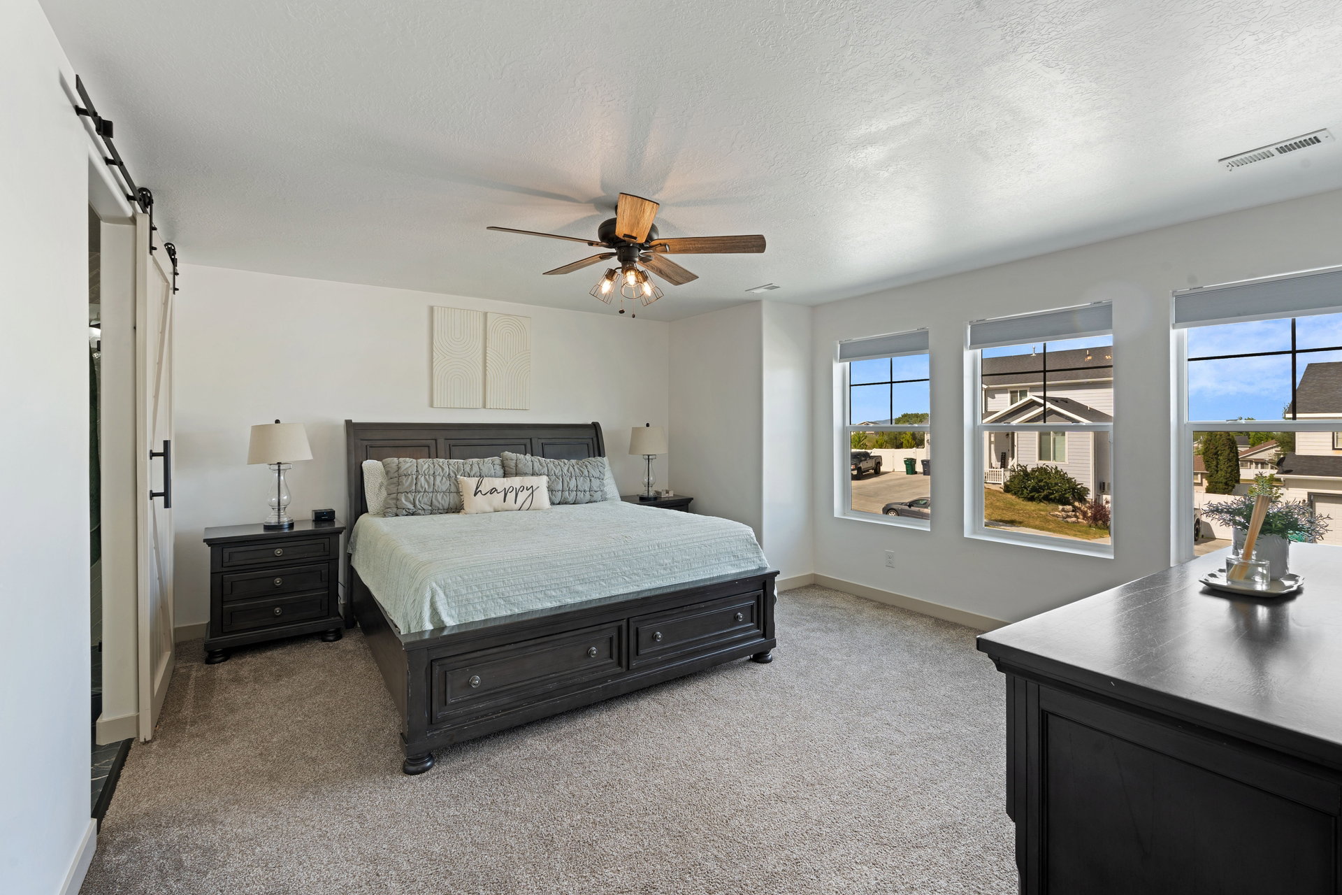 Primary bedroom featuring a ceiling fan with integrated lighting, three large windows, and a white barn door