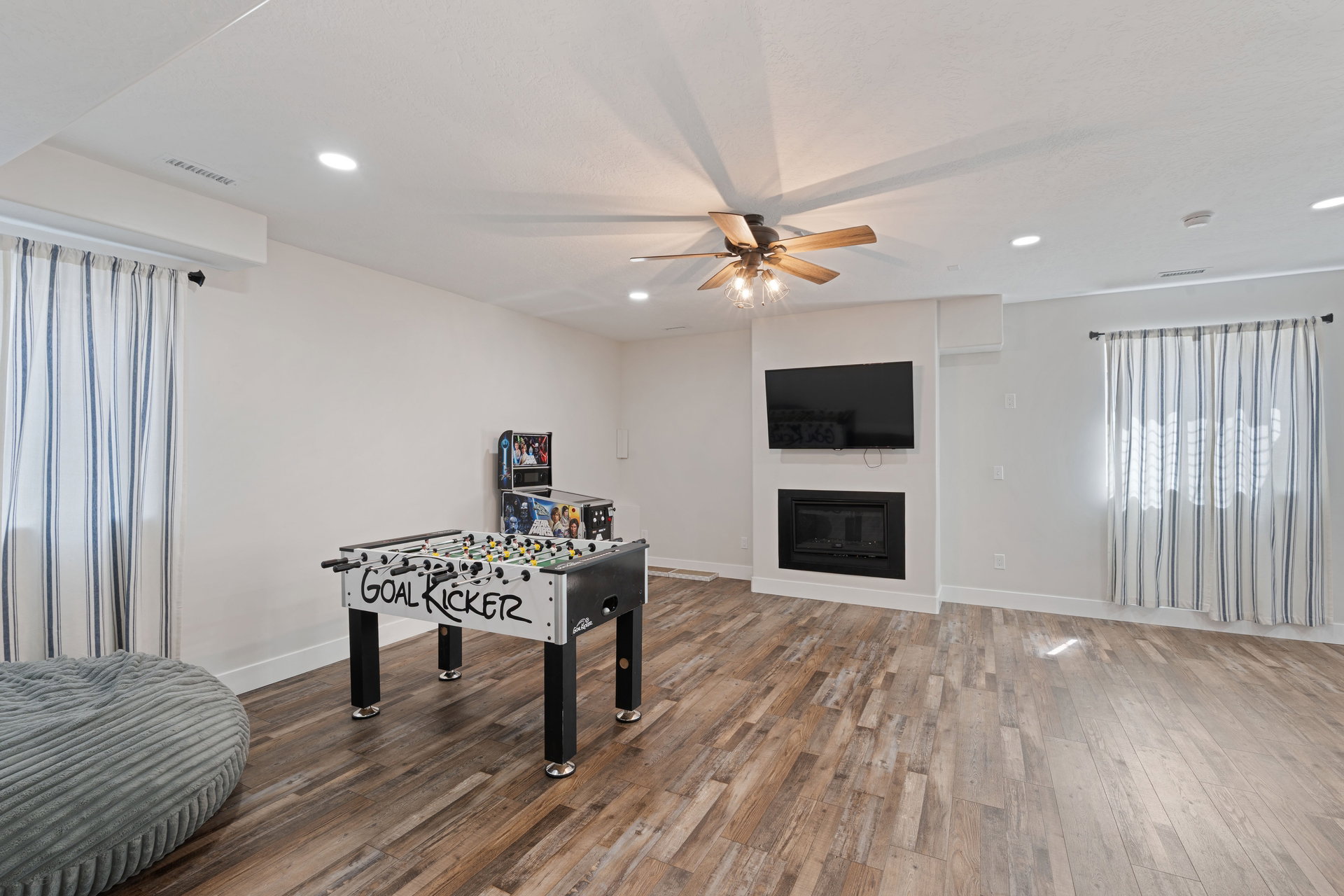 Basement spacious entertainment area featuring wood-finish flooring, a built-in fireplace, a ceiling fan with integrated lighting, and recessed ceiling lights