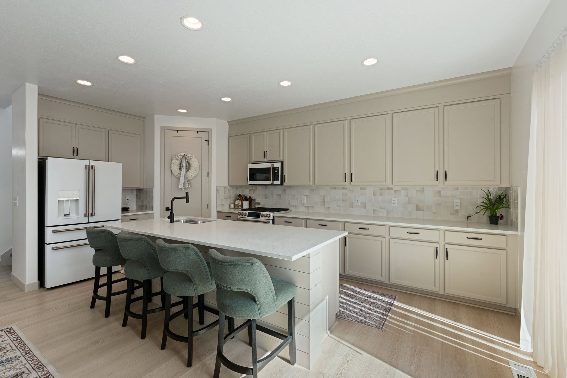Contemporary kitchen featuring a large central island with a solid surface countertop, light cabinetry with dark hardware, a tile backsplash, light wood-finish flooring, and recessed lighting