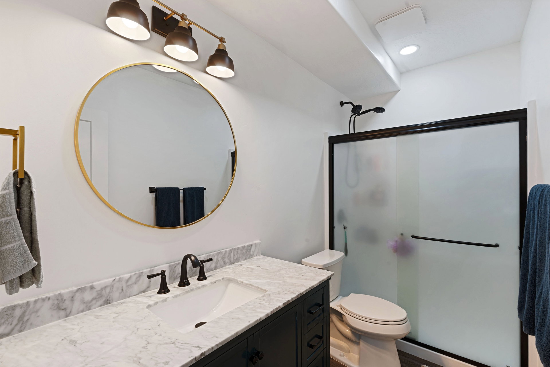 Basement bathroom featuring a dark vanity with a white countertop, an undermount sink, and a circular gold-framed mirror