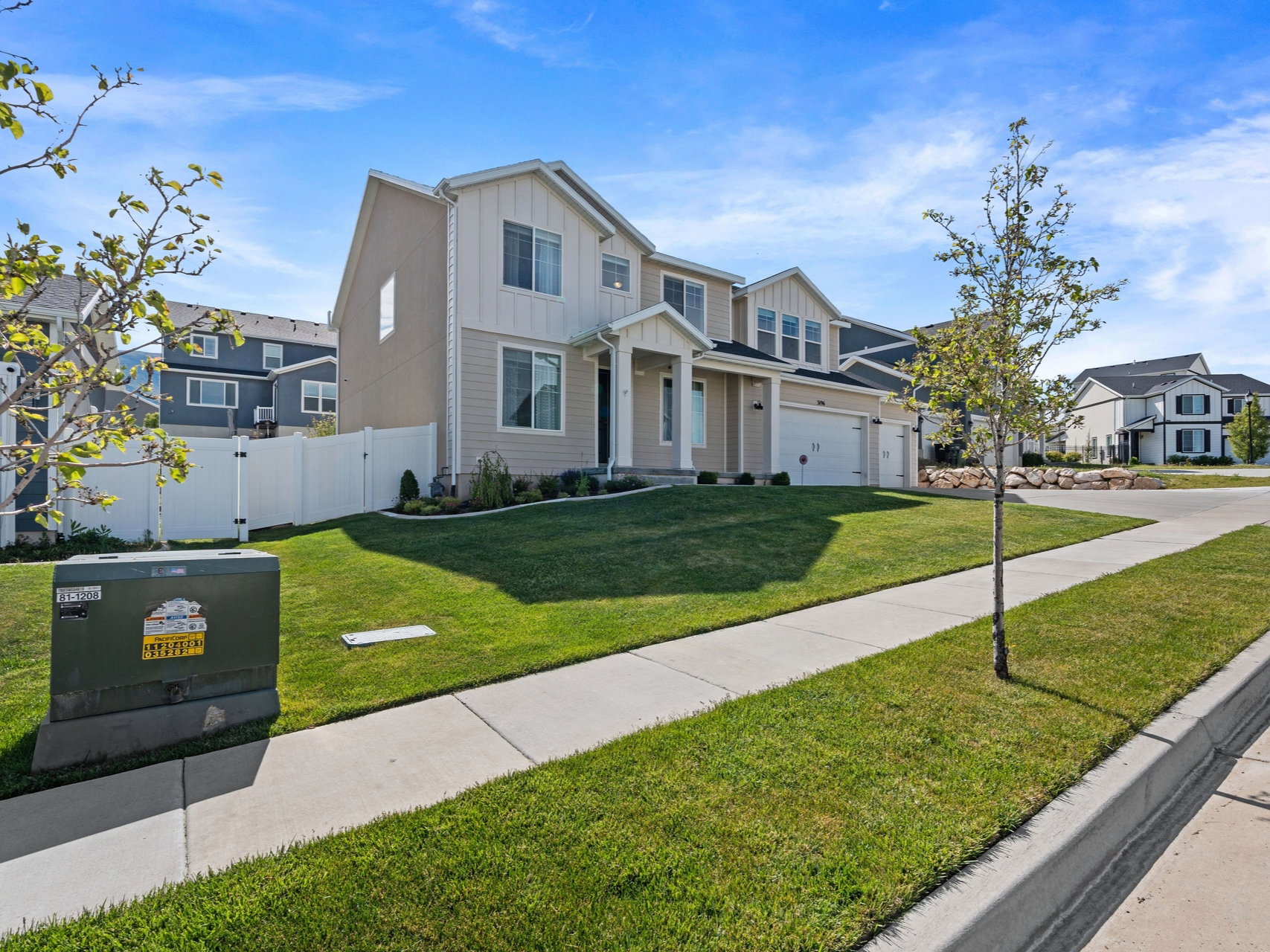 Two-story residence featuring light-toned siding with vertical accents, an attached two-car garage, a covered front entry, and a manicured front lawn with a sidewalk